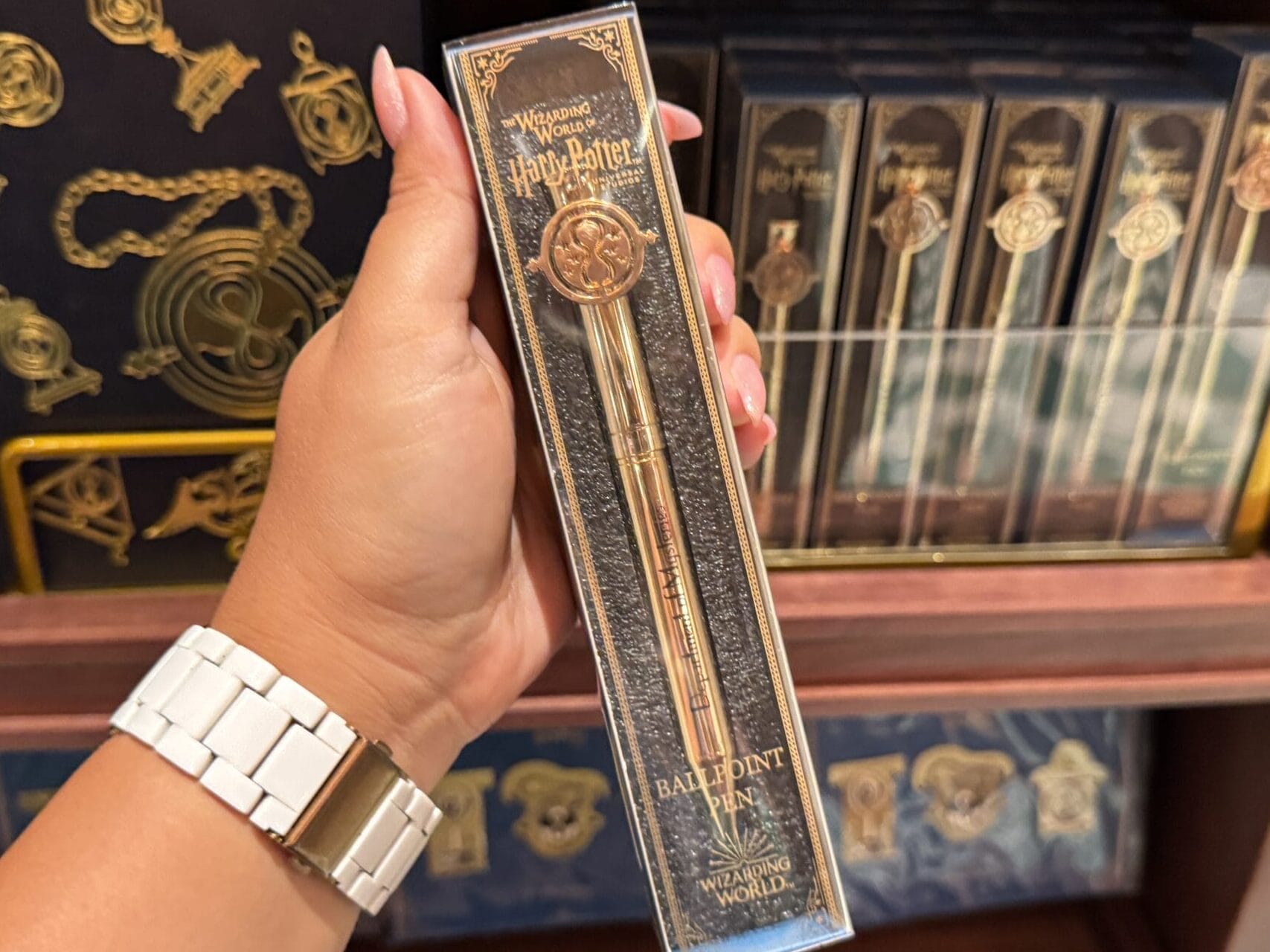 A hand holds a Wizarding World of Harry Potter merchandise wand box in front of shelves filled with themed items.
