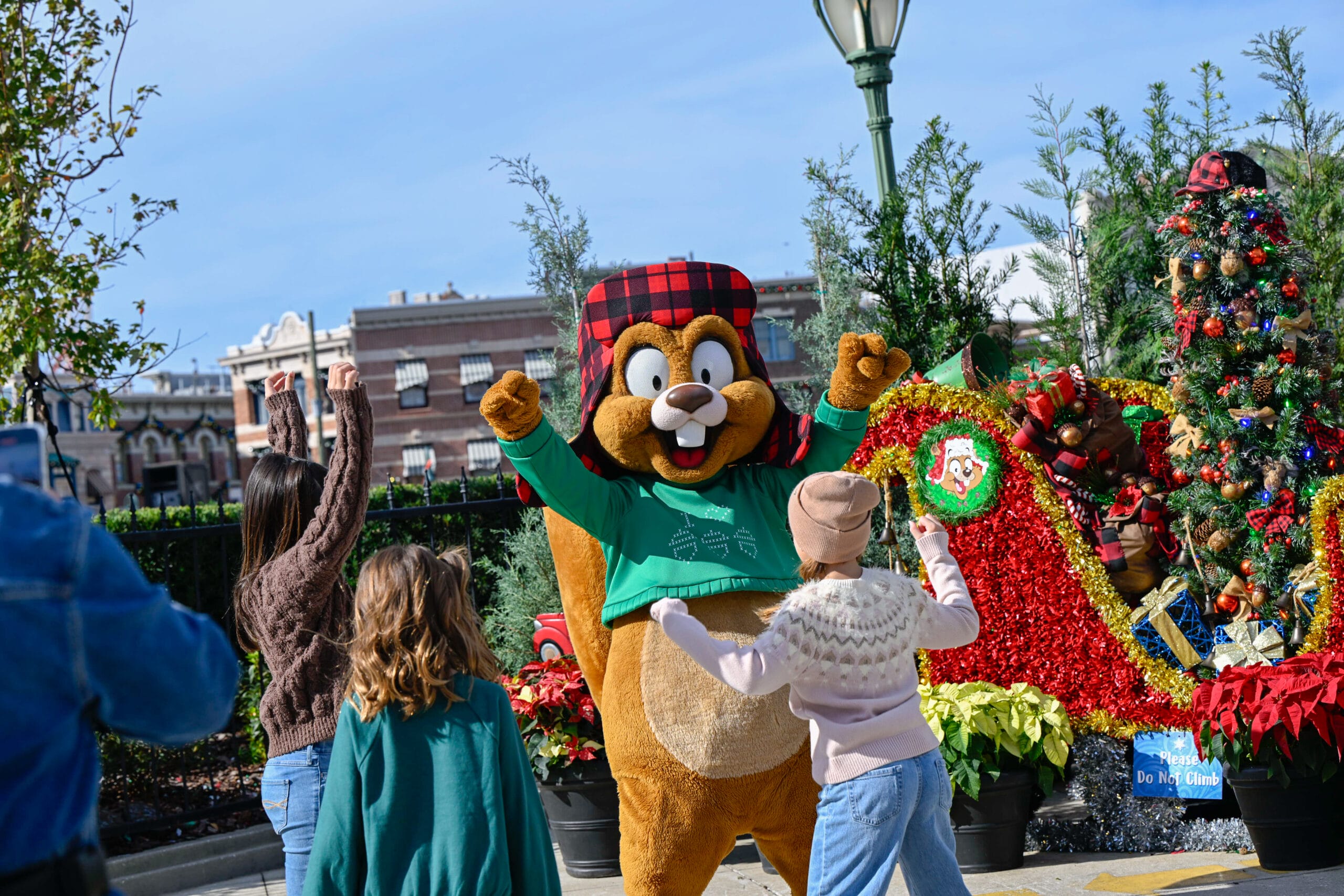 A person in a beaver costume celebrates with kids by a festive sleigh; not like Disney, there’s no castle backdrop here.