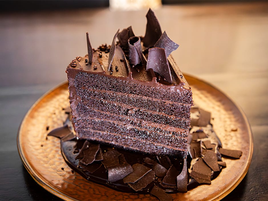 A slice of layered chocolate cake with shavings on a brown plate.