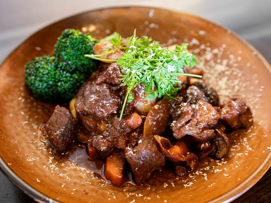 A hearty brown plate of beef stew with carrots, mushrooms, and broccoli