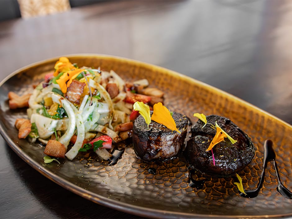 Two pieces of seared meat with edible flowers and salad