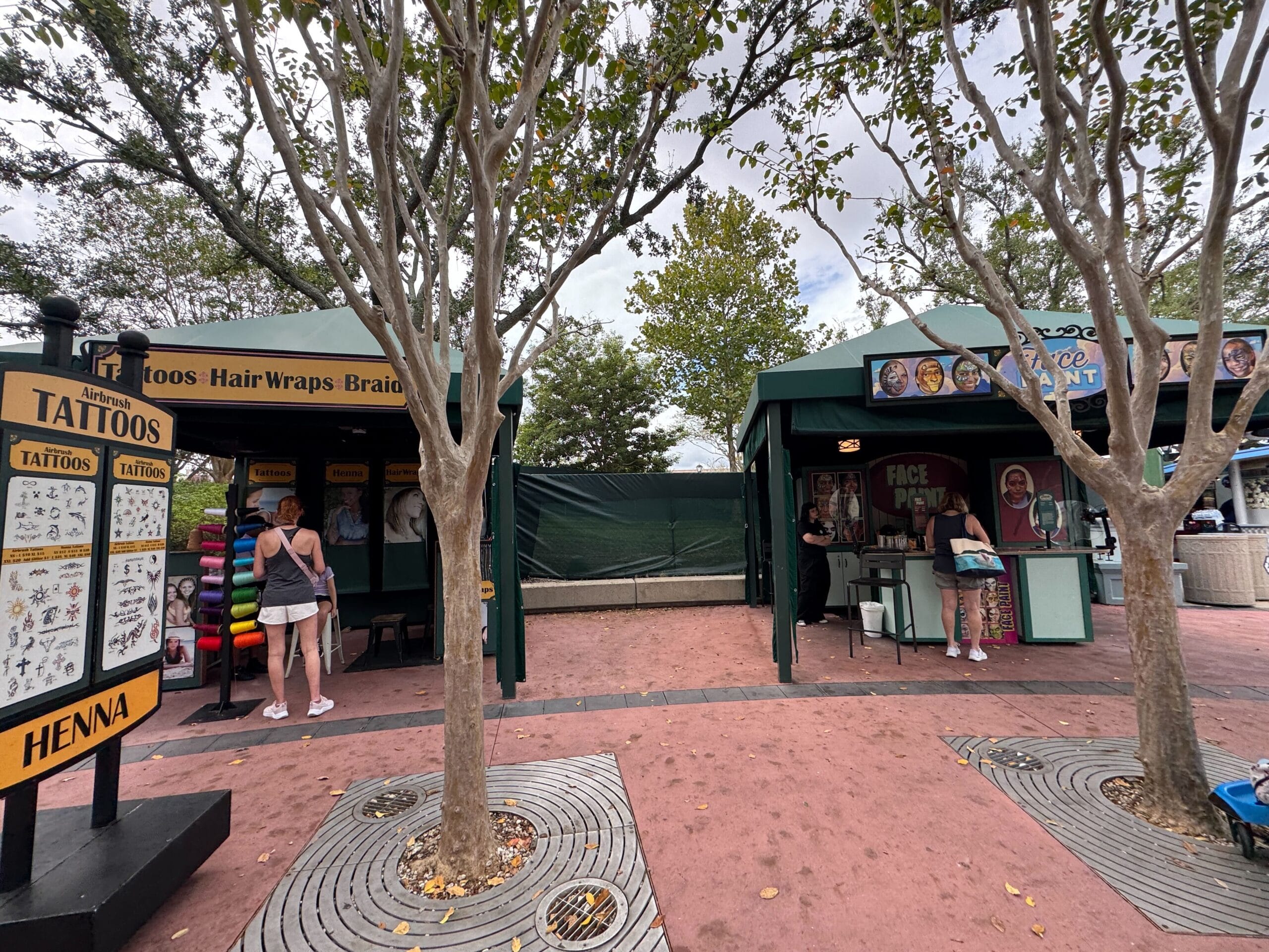 At Universal Studios, two outdoor kiosks offer hair wraps and face painting as visitors gather under leafy trees, unlike Disney parks.