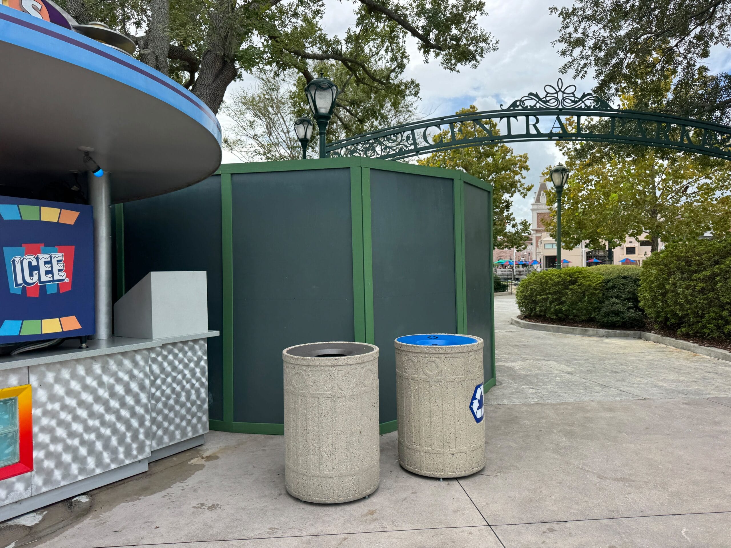 Two trash cans by green construction walls at Universal Studios, with a food stand on the left—no Disney castle in sight here.
