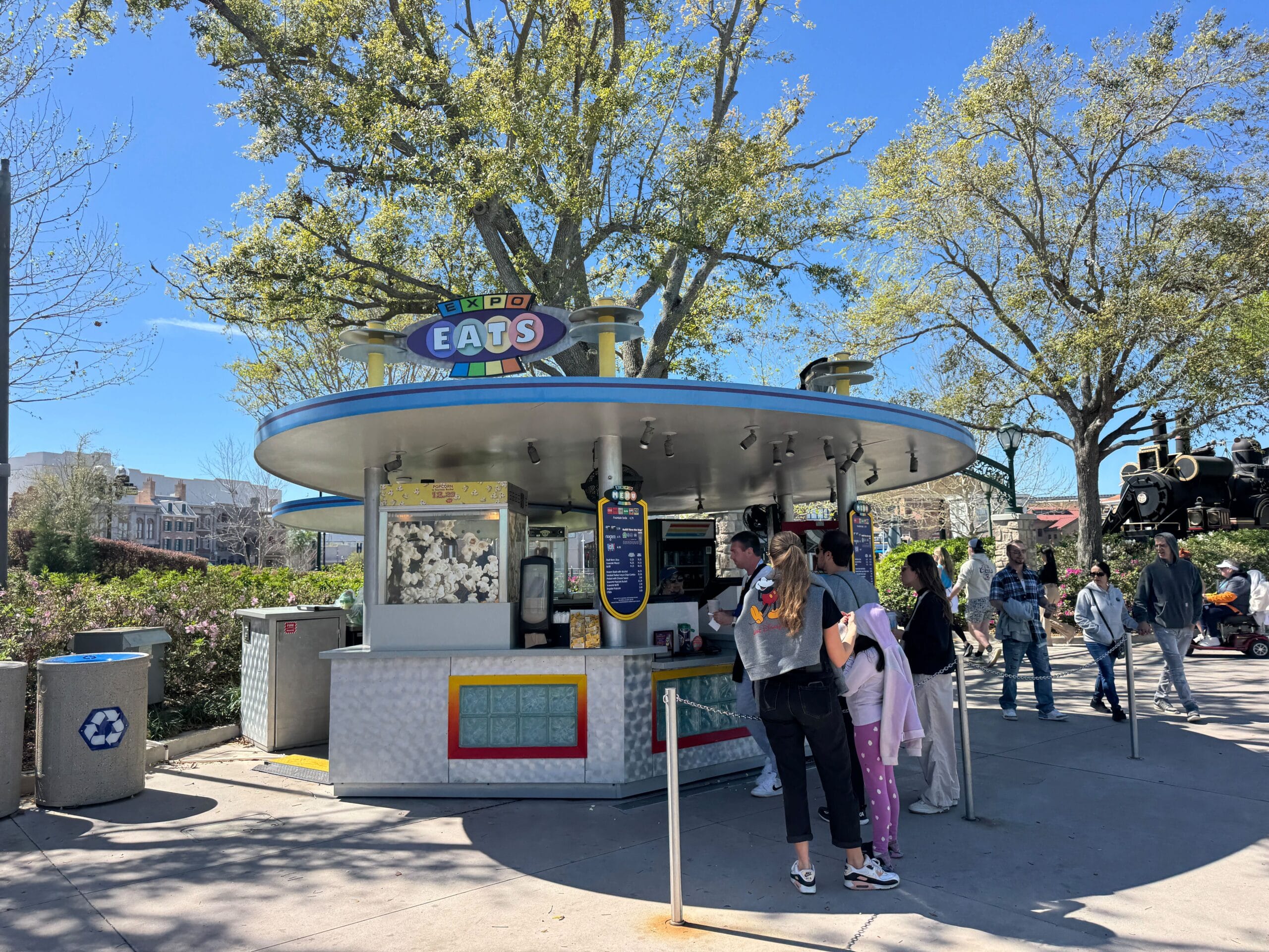Guests queue at the “Eats” snack stand in Universal Studios, with trees and parkgoers nearby—distinct from Disney’s castle areas.