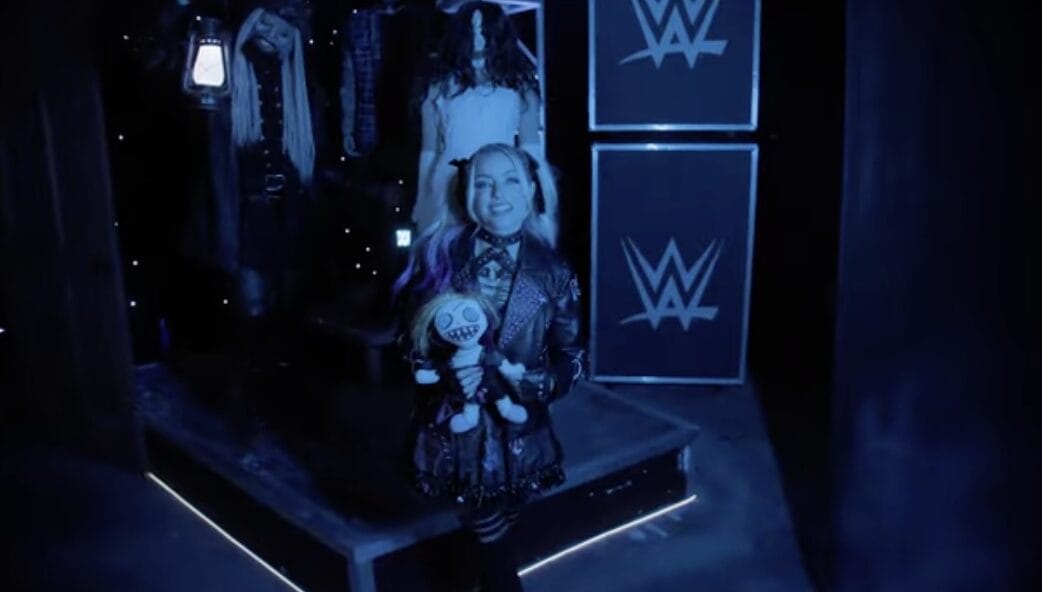 A woman in dark clothes holds a doll in a dim room at Halloween Horror Nights, with spooky mannequins behind—no Disney castle here.