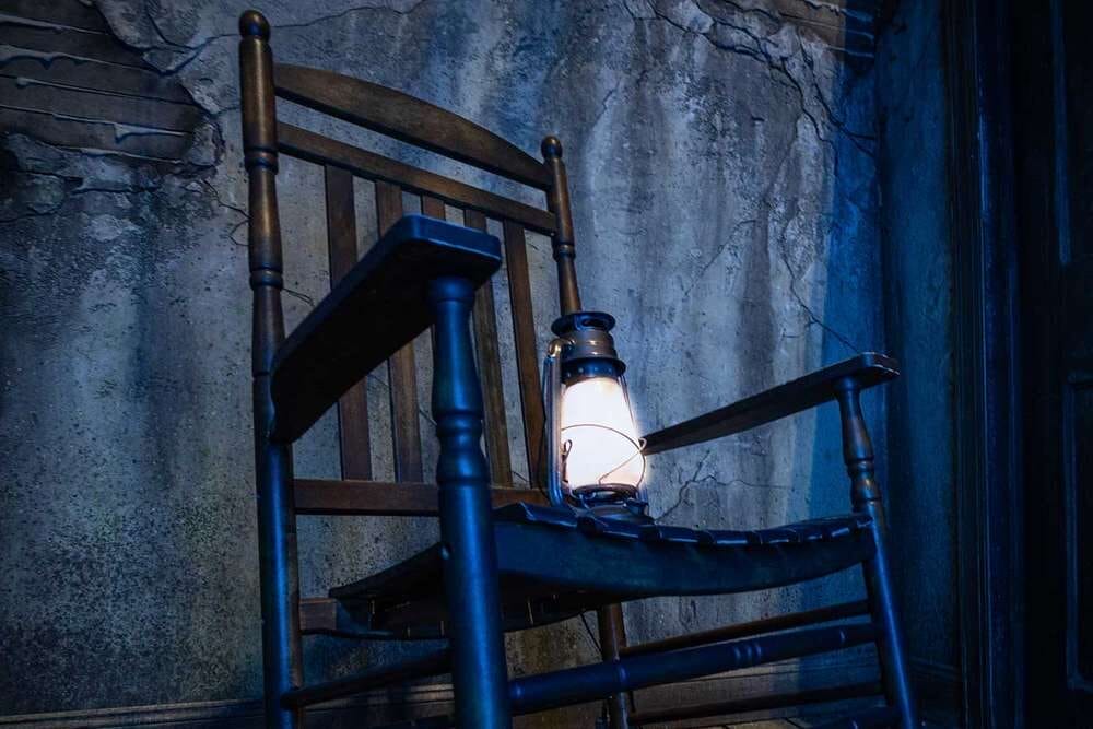 A glowing lantern rests on a rocking chair by a cracked wall, bringing to mind more Haunted Mansion than Sleeping Beauty Castle vibes.