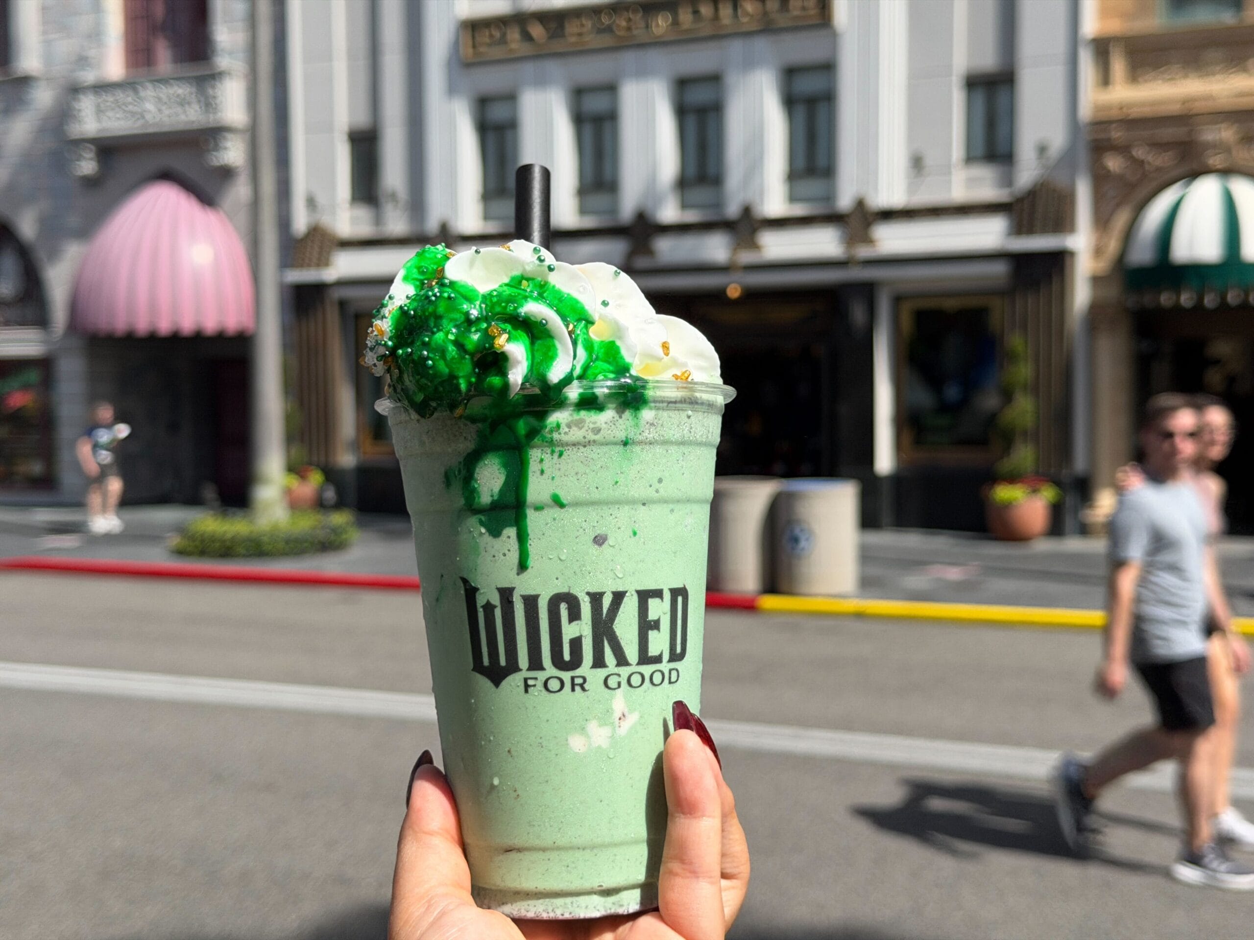A hand holds a green "Wicked For Good" milkshake at Universal Studios Florida, though this celebration isn’t at a Disney park or castle.