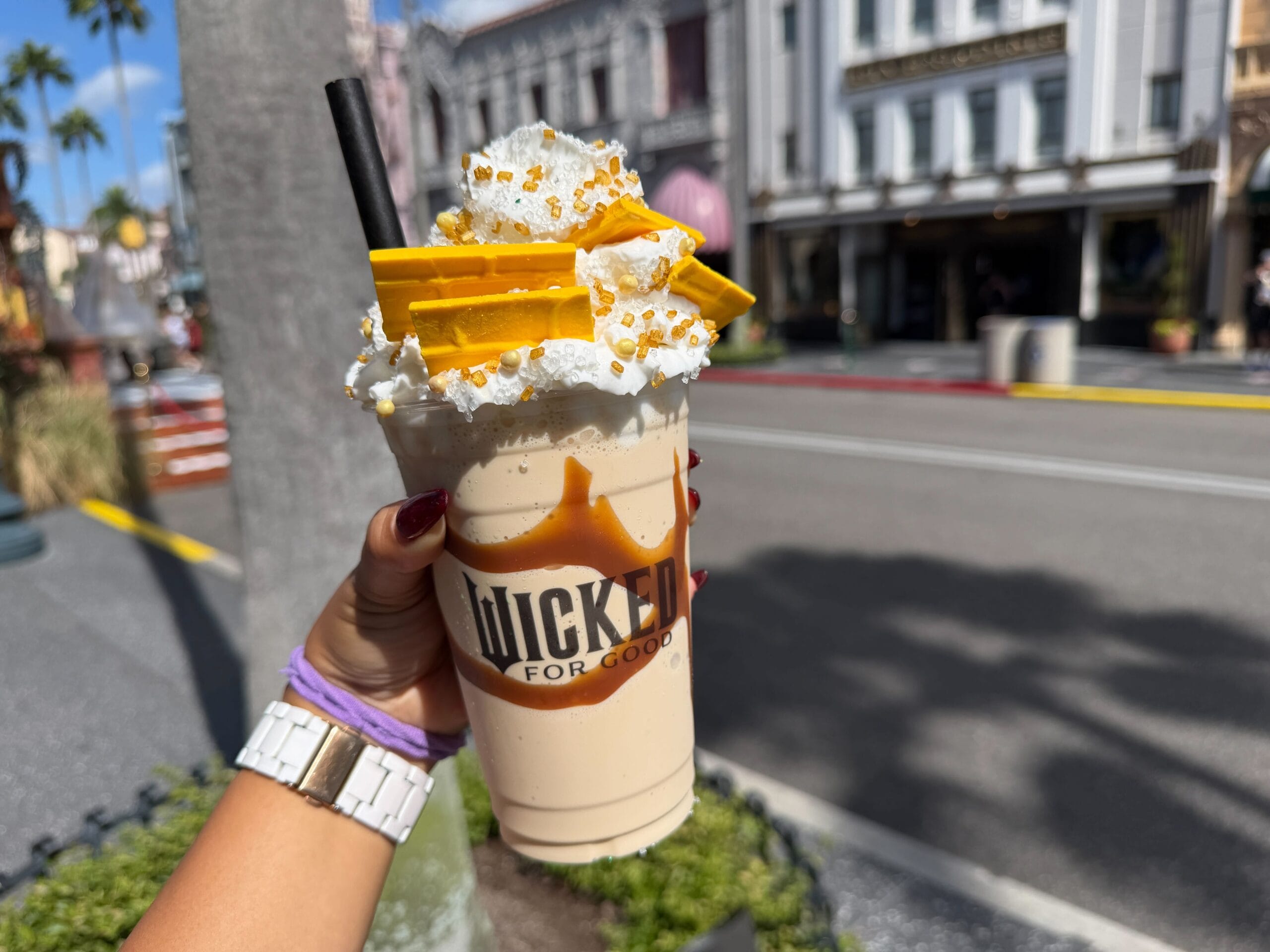 A hand holds a Wicked caramel milkshake topped with whipped cream and yellow chocolate, but unlike Disney's castle treats, it's at Universal.