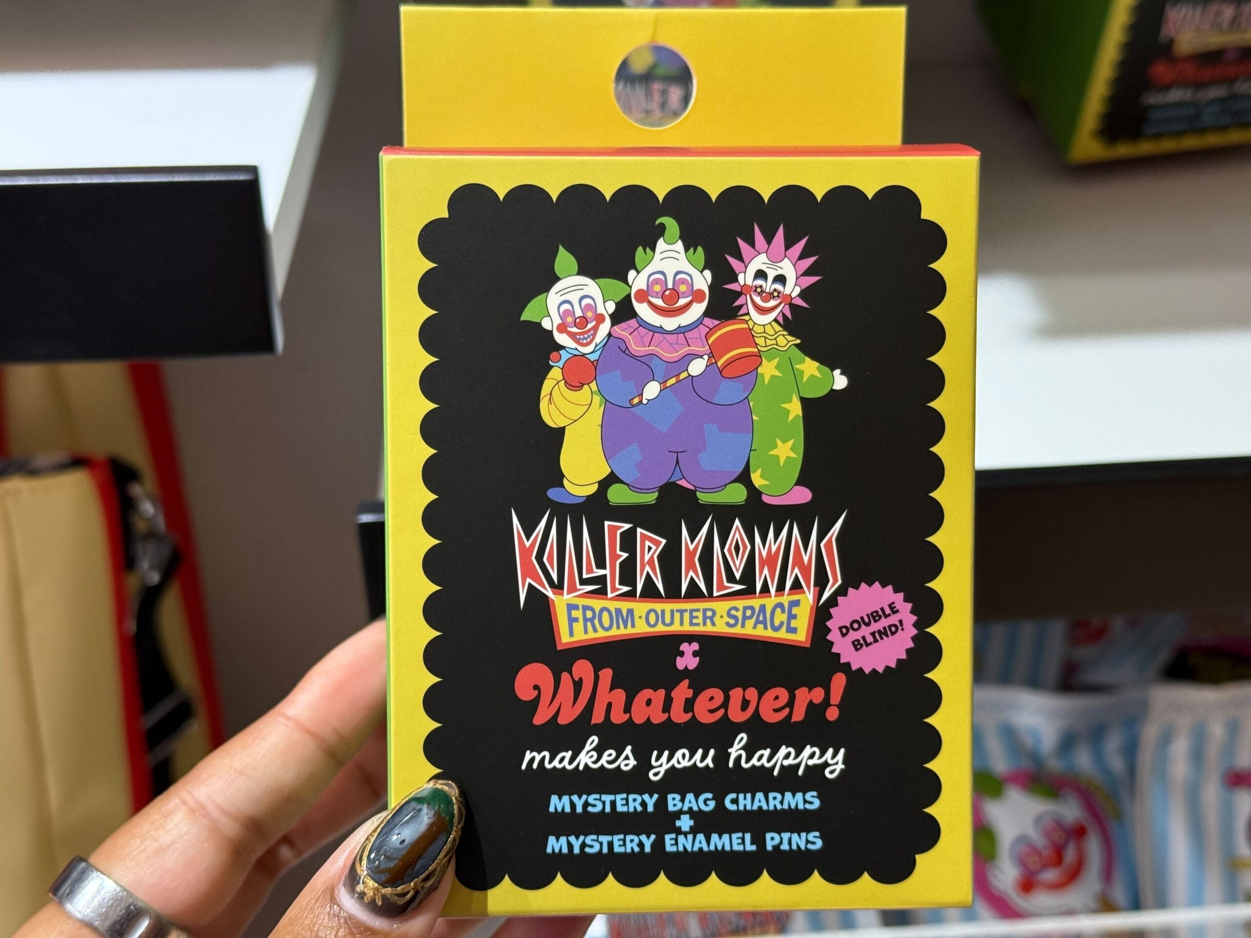 A hand shows a "Killer Klowns from Outer Space" mystery bag charm and enamel pin box at Universal Studios.