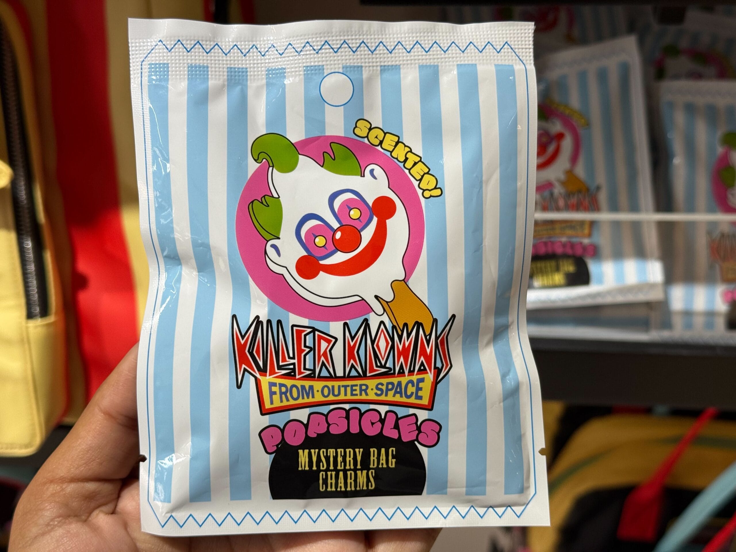 A hand shows a "Killer Klowns from Outer Space" popsicle mystery bag charm pouch at Universal Studios.