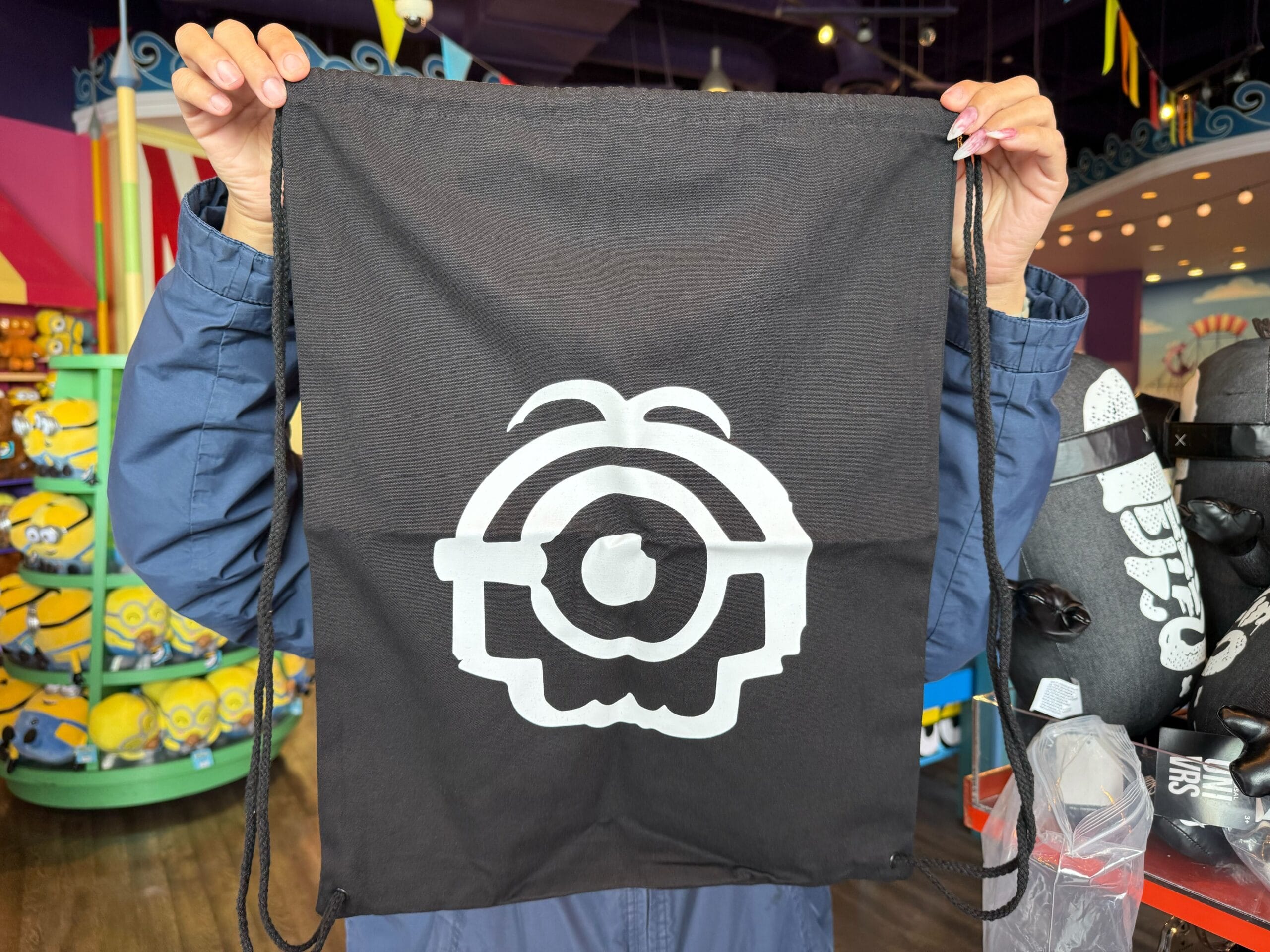 Person holding a black Emo Minion Merchandise bag in a vibrant theme park store, unlike the Disney castle shops at Disneyland.