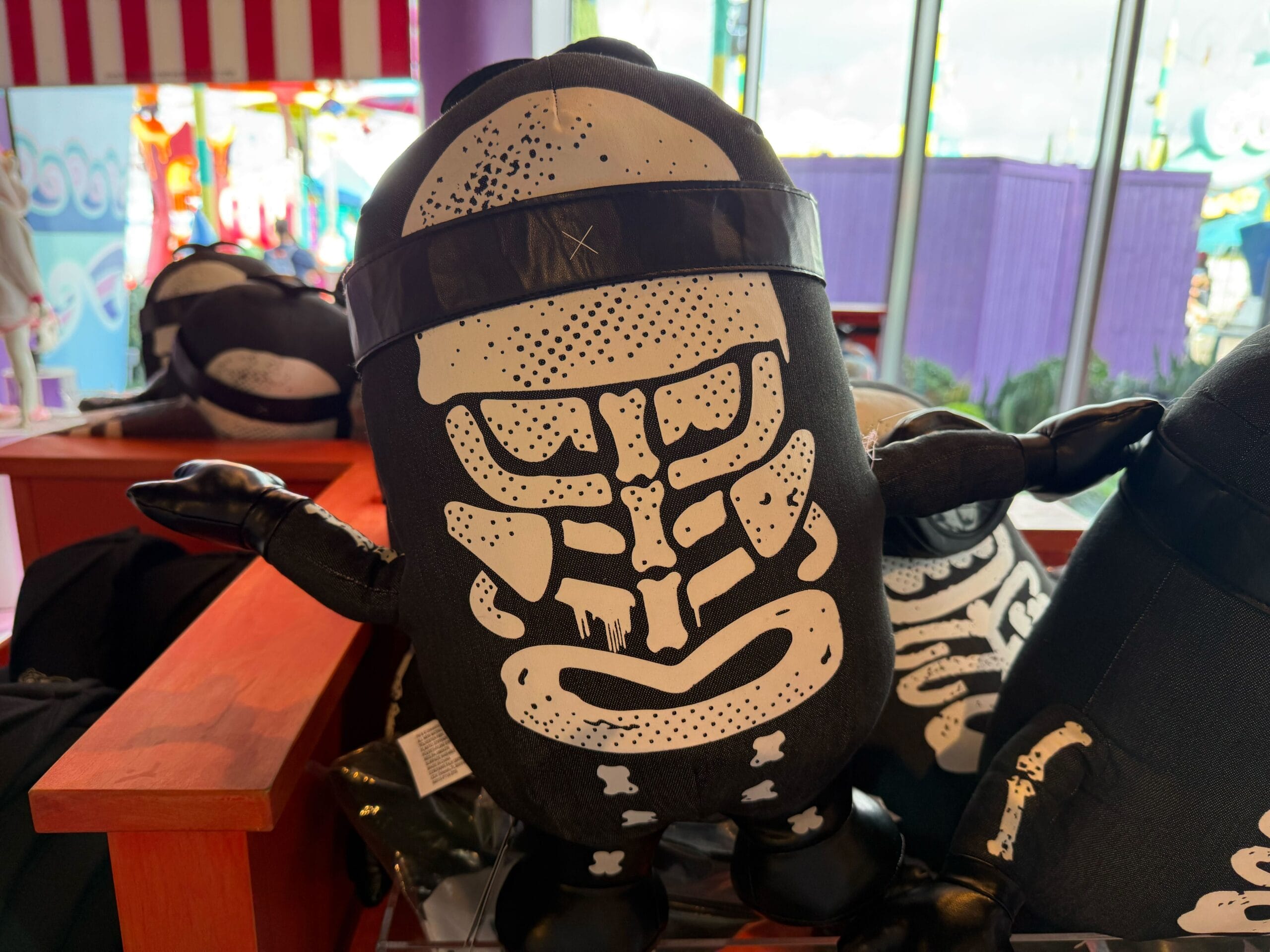 An Emo Minion plush with a white skeleton design sits on a wooden shelf, not far from castle icons like Disneyland’s Sleeping Beauty Castle.
