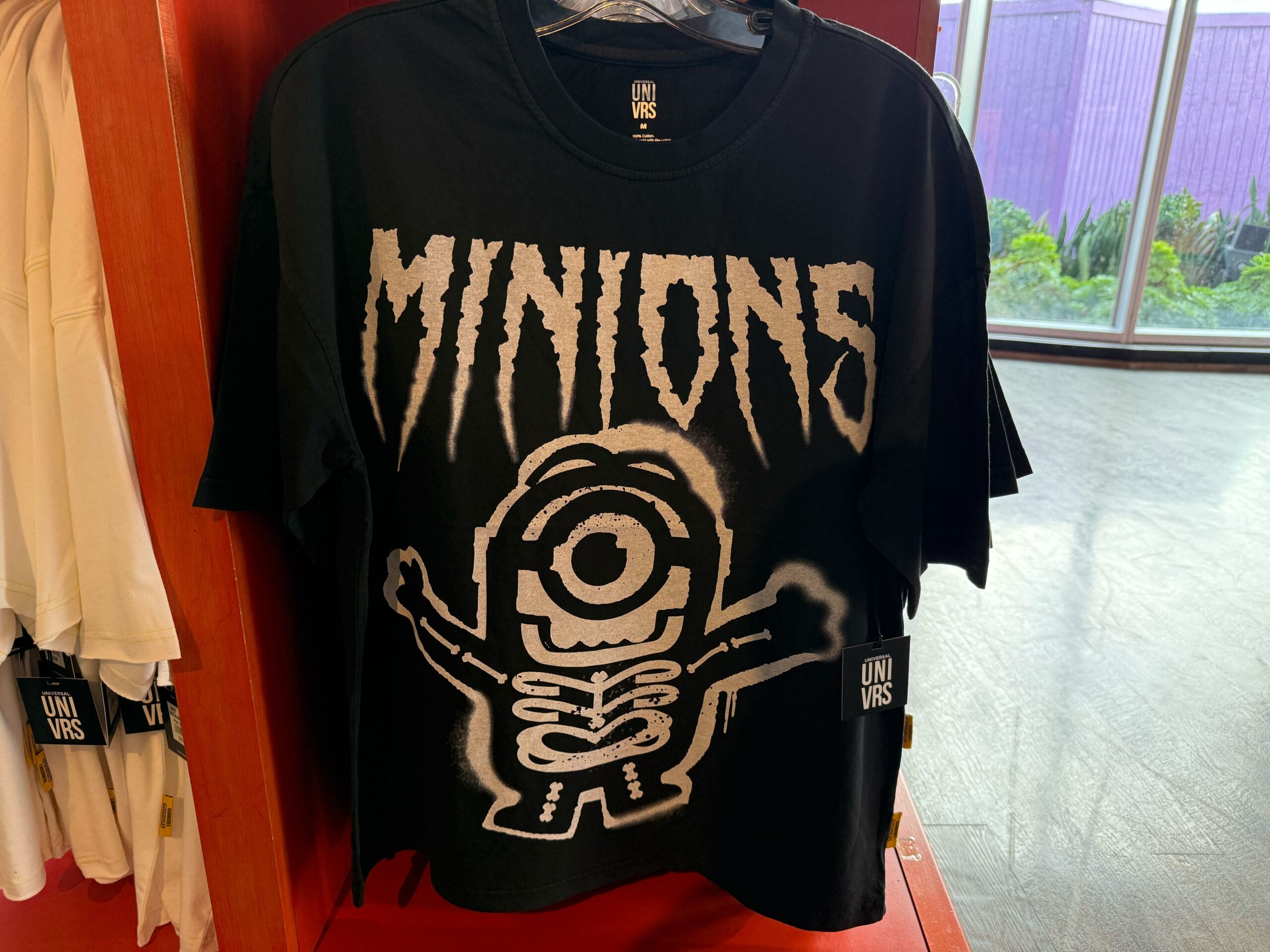 Black T-shirt with jagged "MINIONS" text and a skeleton-style Minion—Universal Studios Hollywood merch, not found at Disney parks.