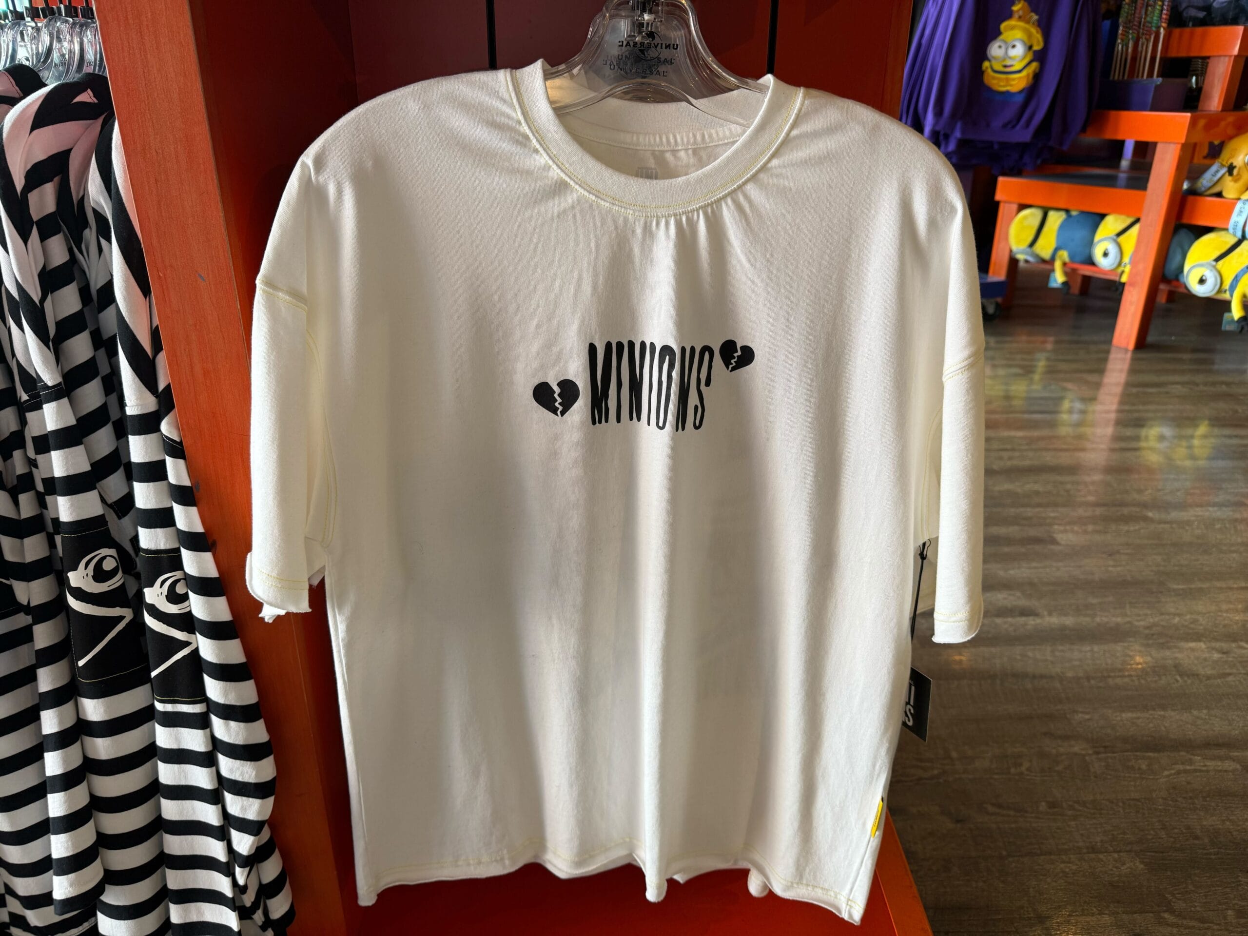 White t-shirt with "MINIONS" text and black hearts—cute Emo Minion merch at Universal Studios, not at any Disney park castle location.