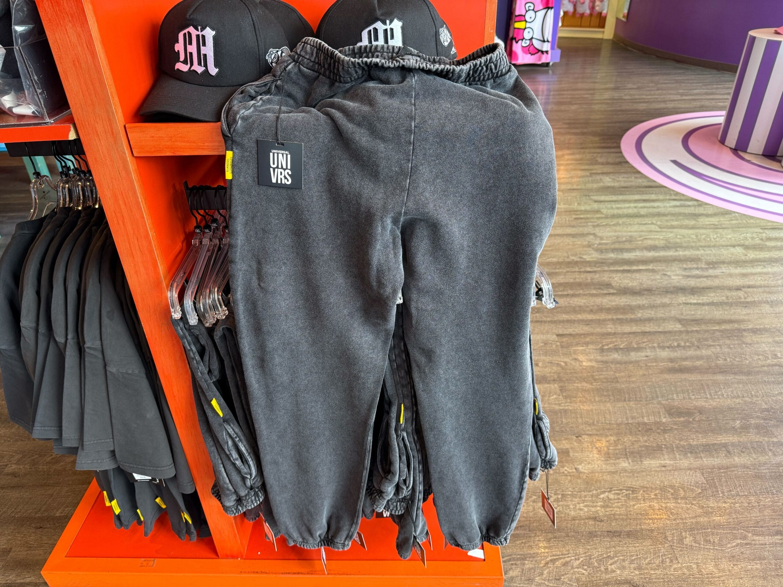 Acid-wash black jogger pants with "UNIVRS" tag, shown near Emo Minion merch in a shop—unlike Disney castle shops’ usual style.