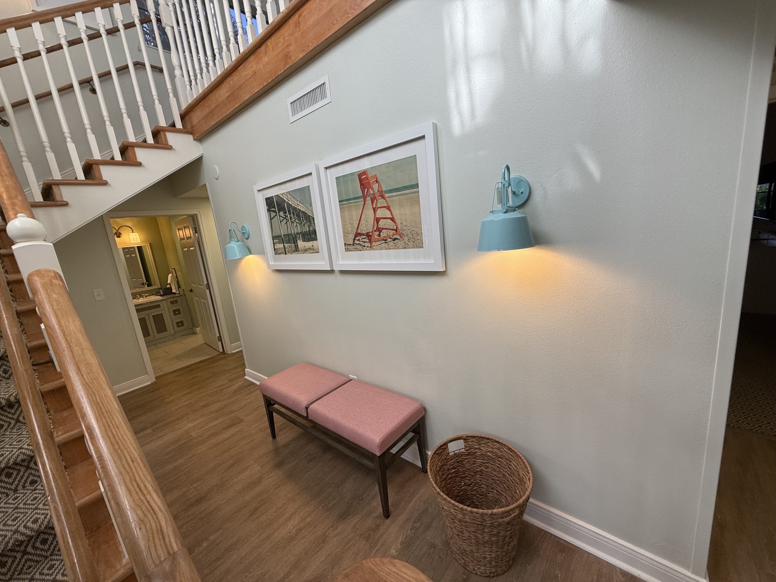 A hallway at Disney’s Vero Beach Resort featuring beach-themed art, blue lamps, a pink bench, and staircase—no castle in view.
