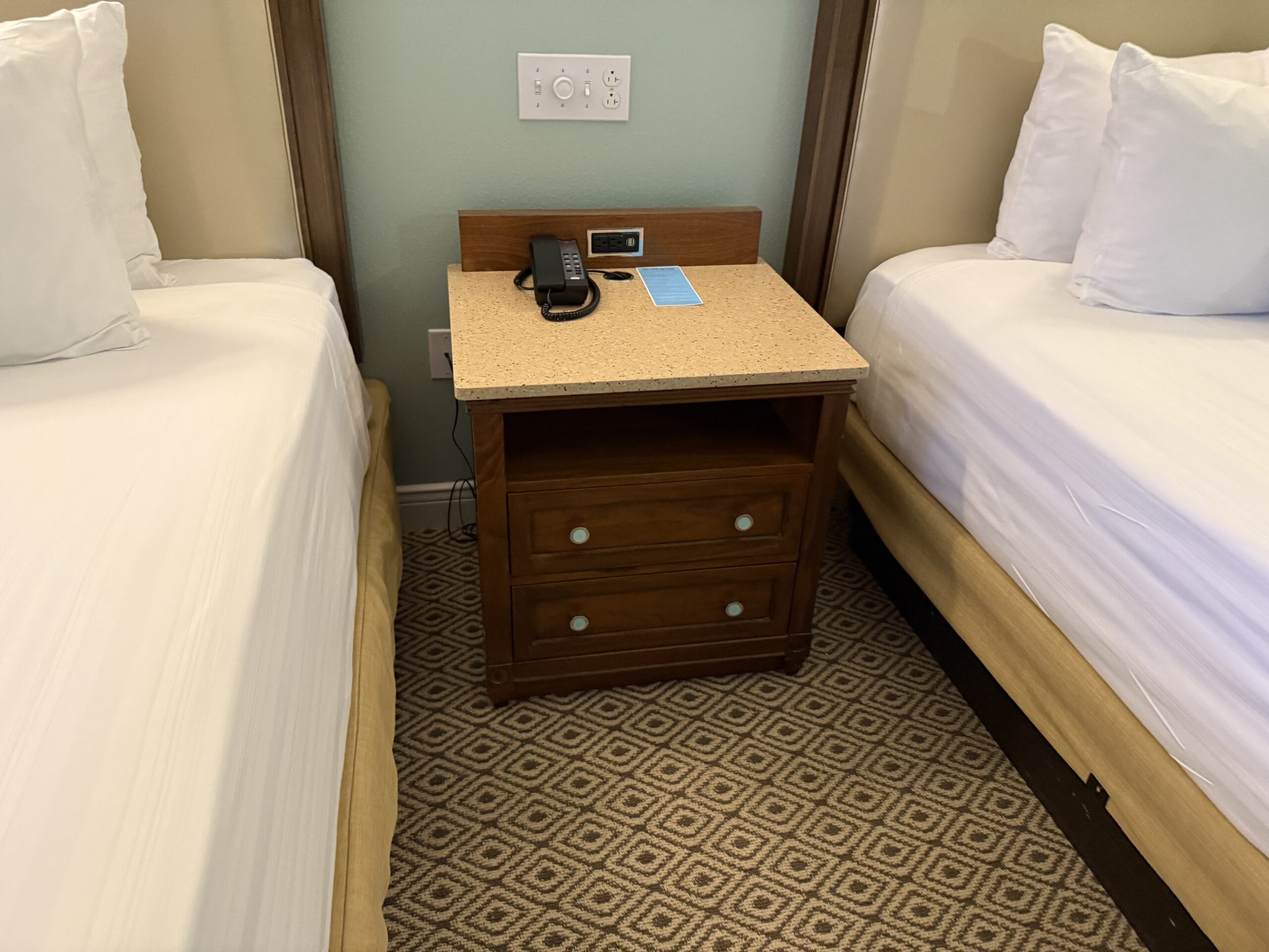 Wooden nightstand with two drawers between beds in a 3-Bedroom Cottage at Disney's Vero Beach Resort, styled for Disney magic.