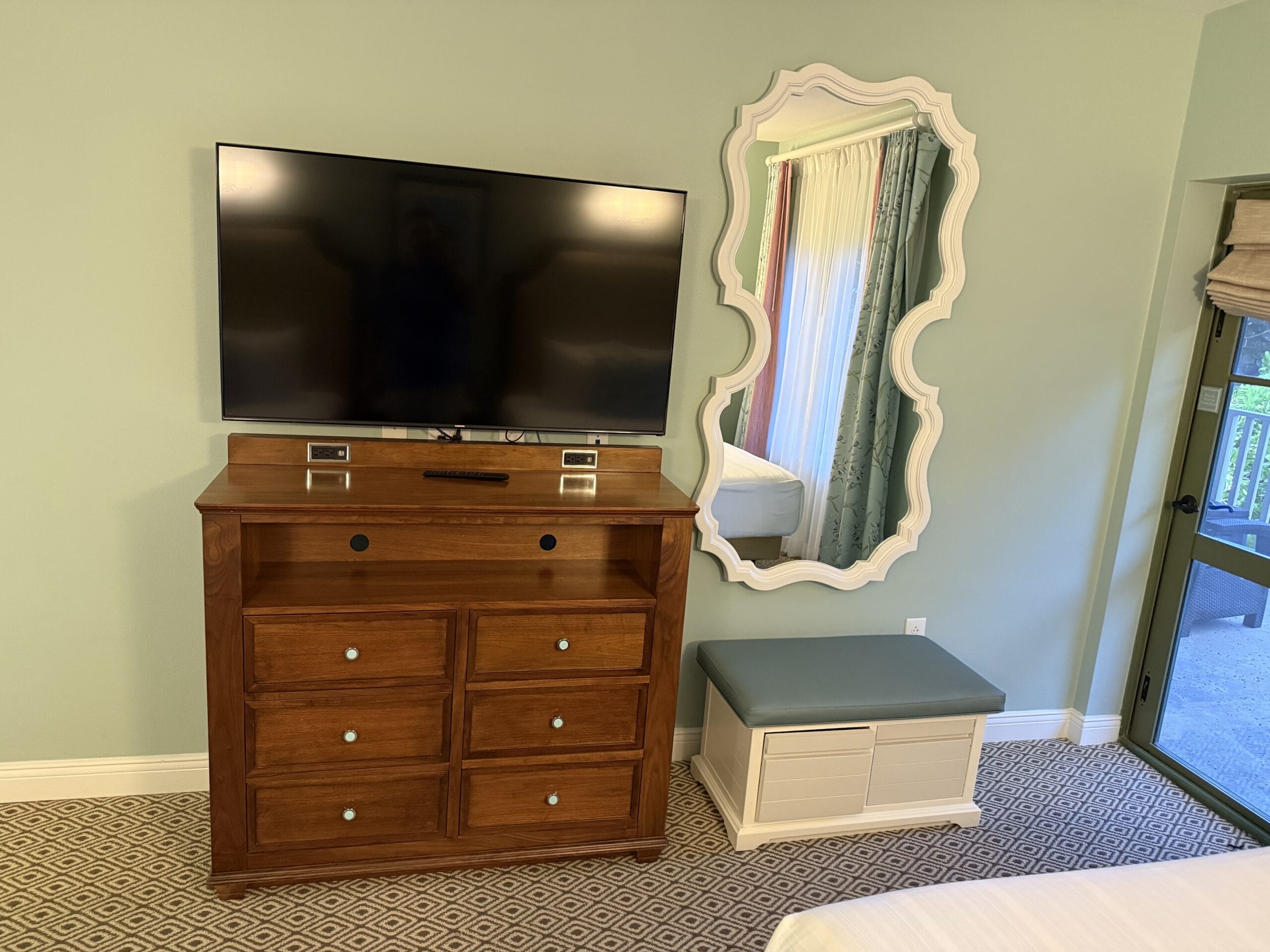 Flat-screen TV on wooden dresser, patterned carpet, ornate mirror in Disney's Vero Beach Resort 3-bedroom cottage—no castle view.