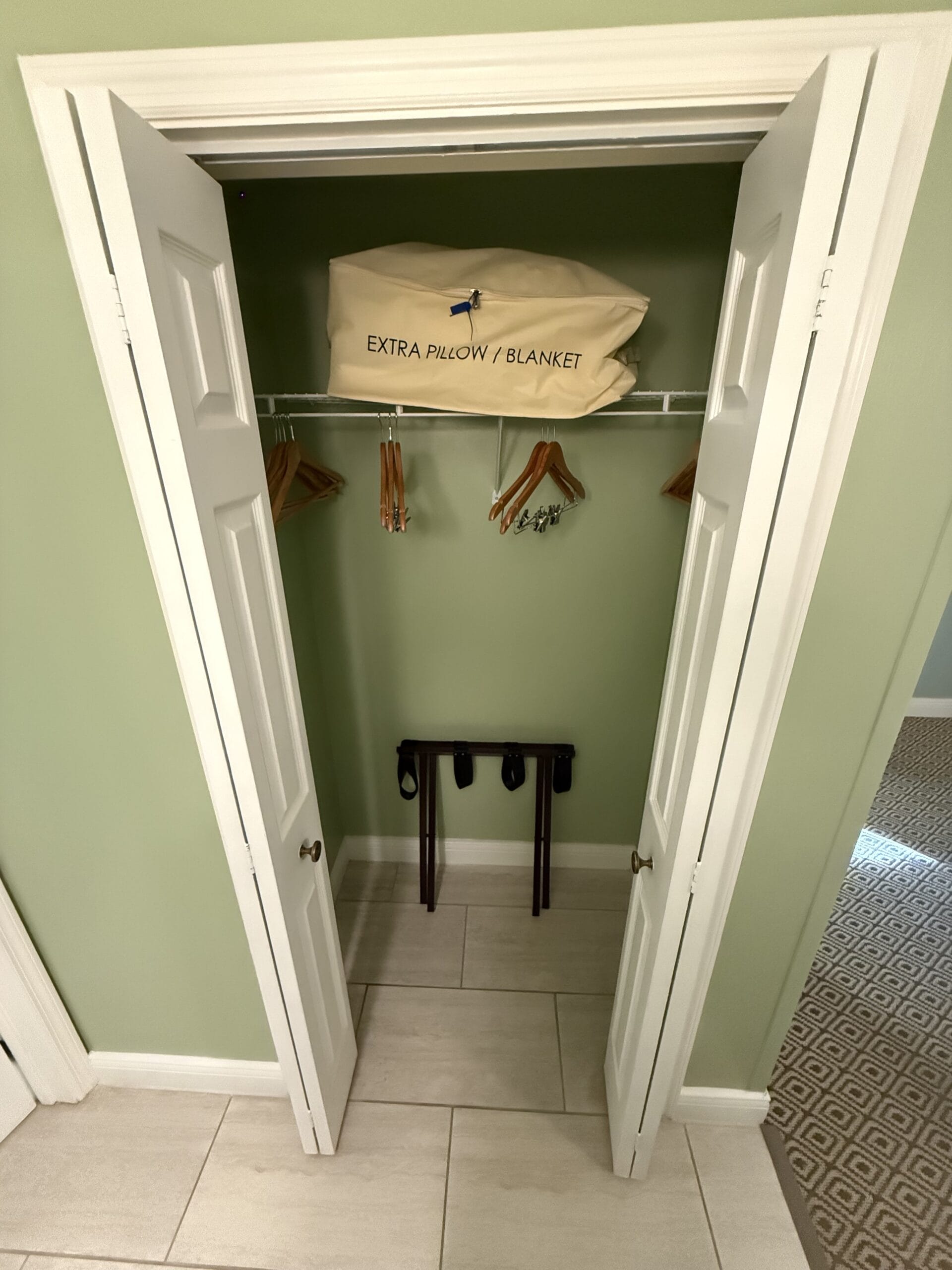 Open closet in 3 Bedroom Cottage at Disney's Vero Beach Resort with hangers, luggage rack, and an "Extra Pillow/Blanket" bag.