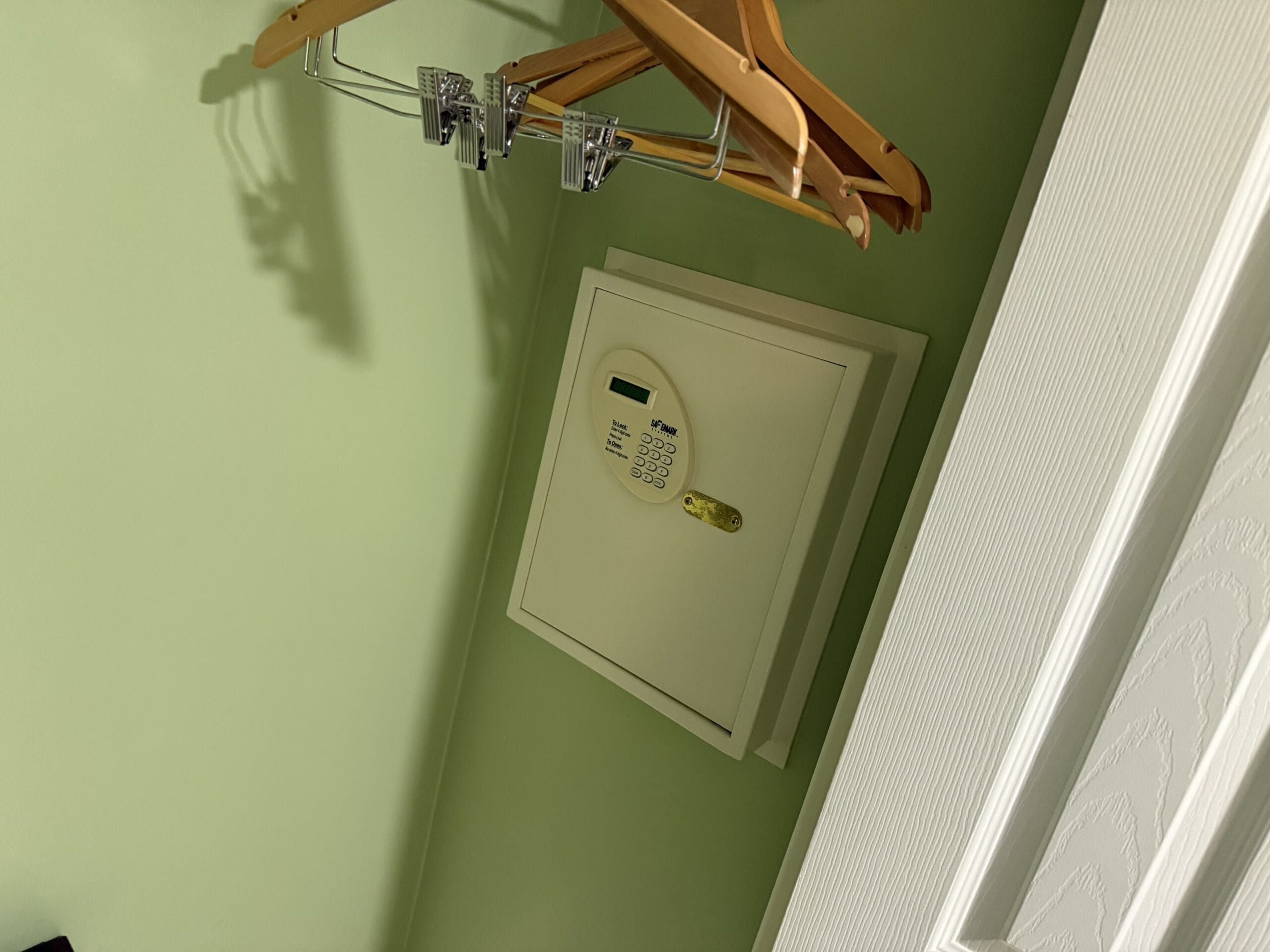 Wall-mounted keypad safe beneath wooden hangers in a green closet at Disney's Vero Beach Resort 3 Bedroom Cottage.