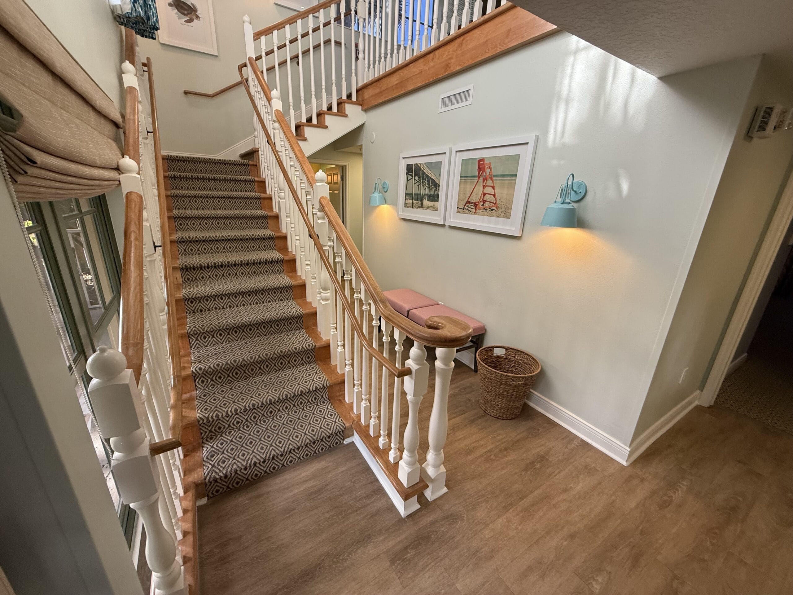 A bright hallway at Disney’s Vero Beach Resort 3 Bedroom Cottage with a carpeted staircase, white railings, art, and a bench.