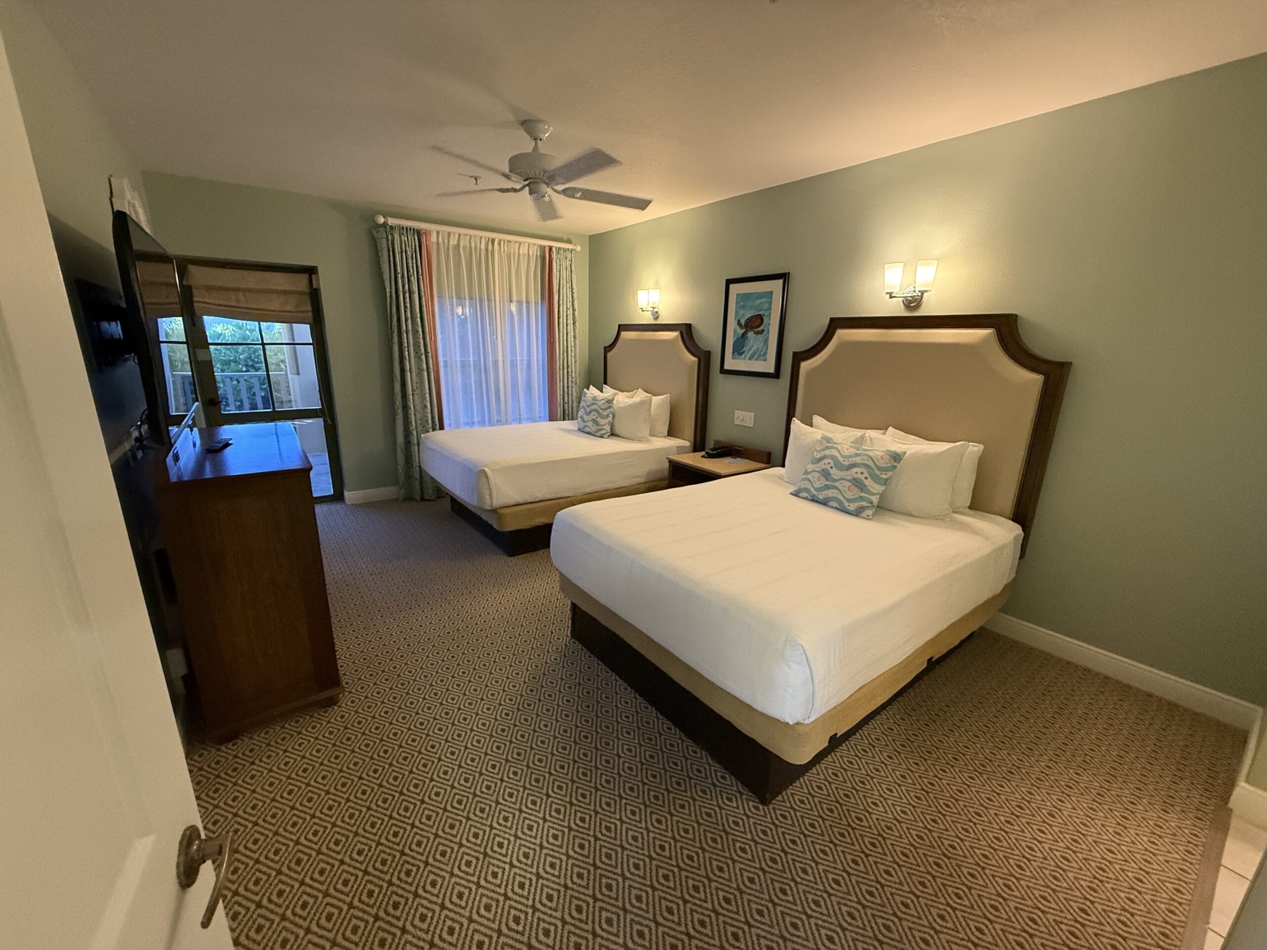Disney's Vero Beach Resort hotel room with two double beds, a dresser, TV, and light green walls—no castle view like at Disney parks.