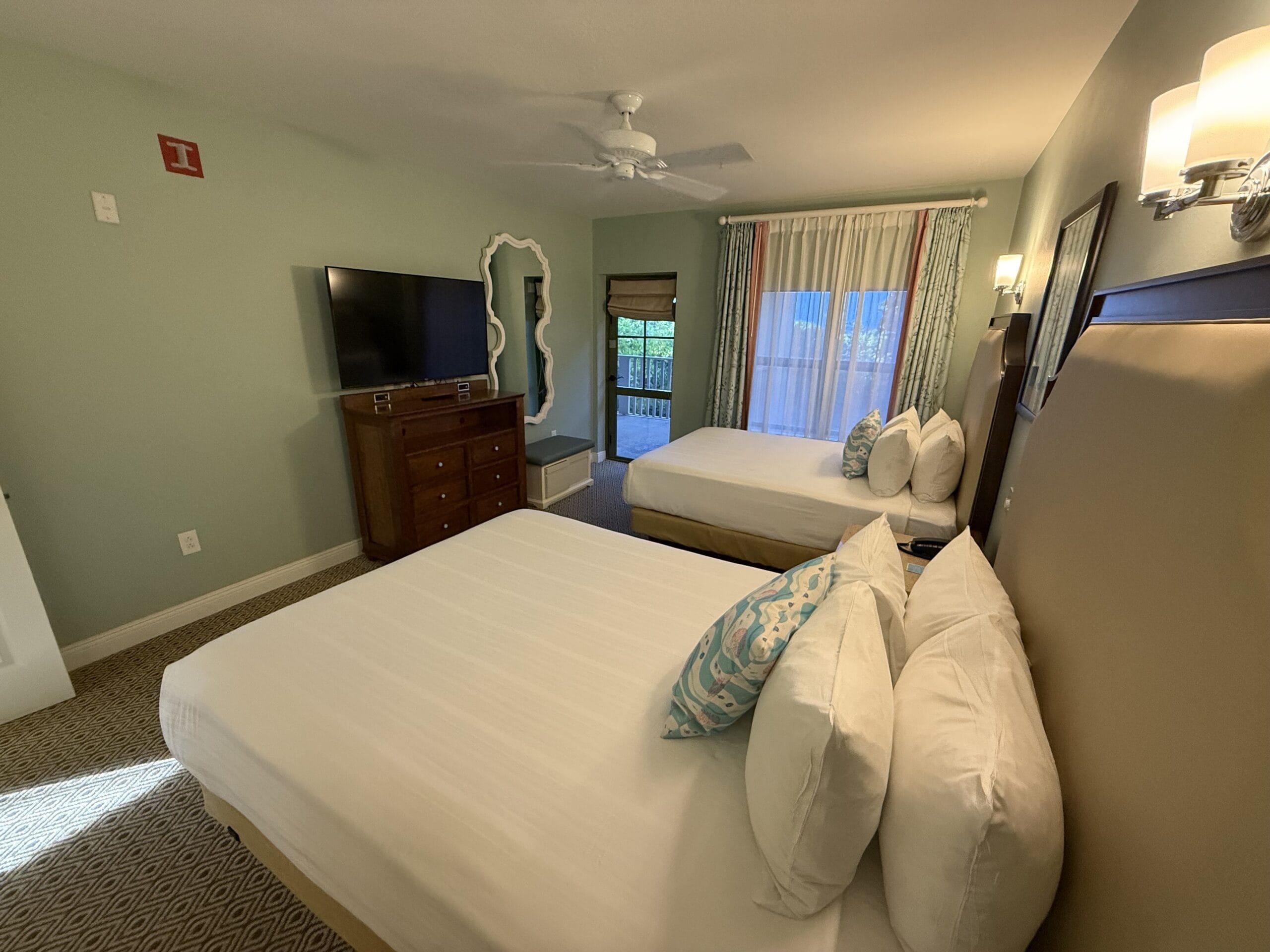 Spacious hotel room at Disney's Vero Beach Resort, featuring two beds, TV, mirror, and balcony, designed with Disney park charm.