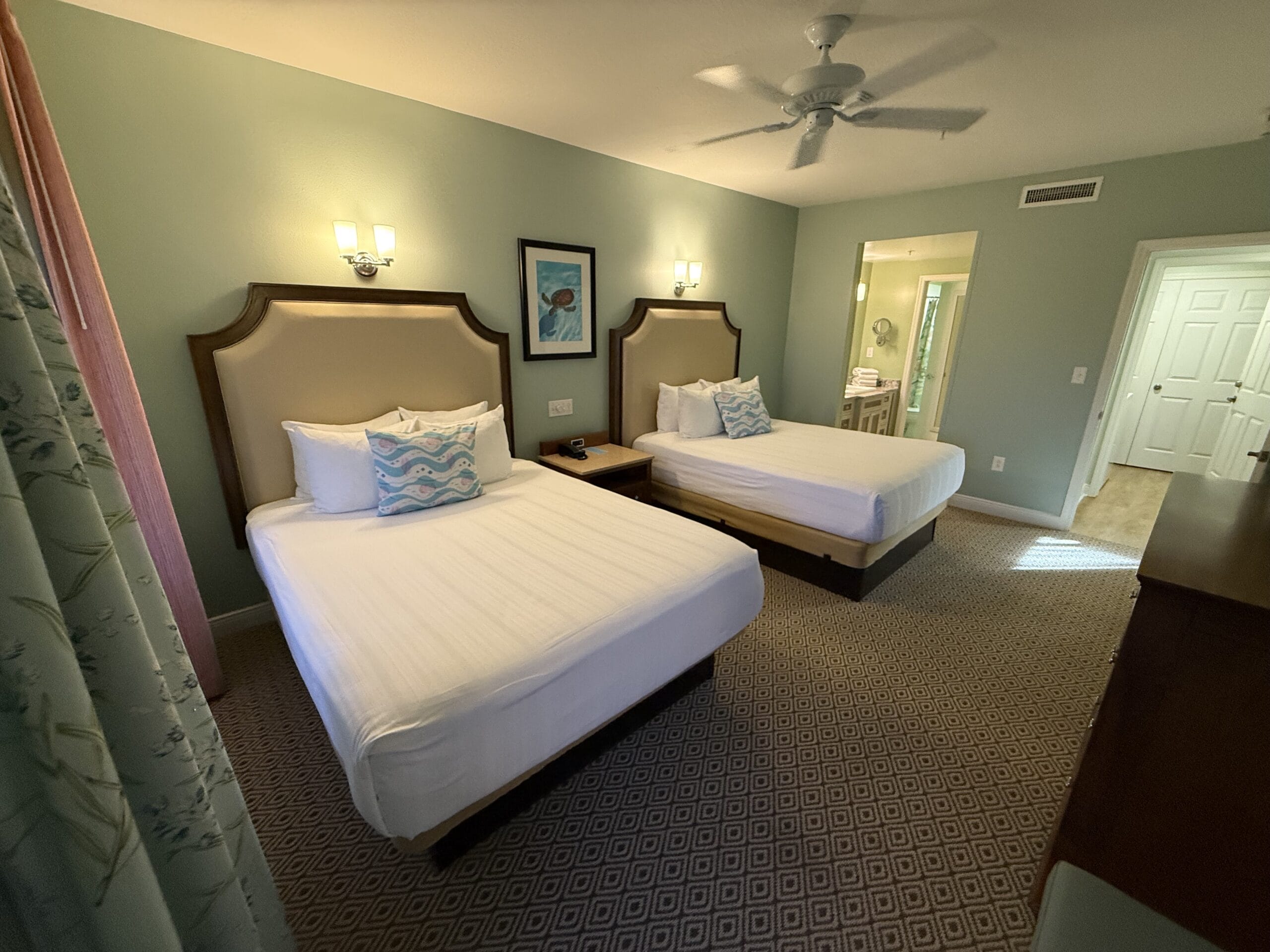 Hotel room at Disney’s Vero Beach Resort with two double beds and green walls—no castle view like Walt Disney World’s, bathroom visible.