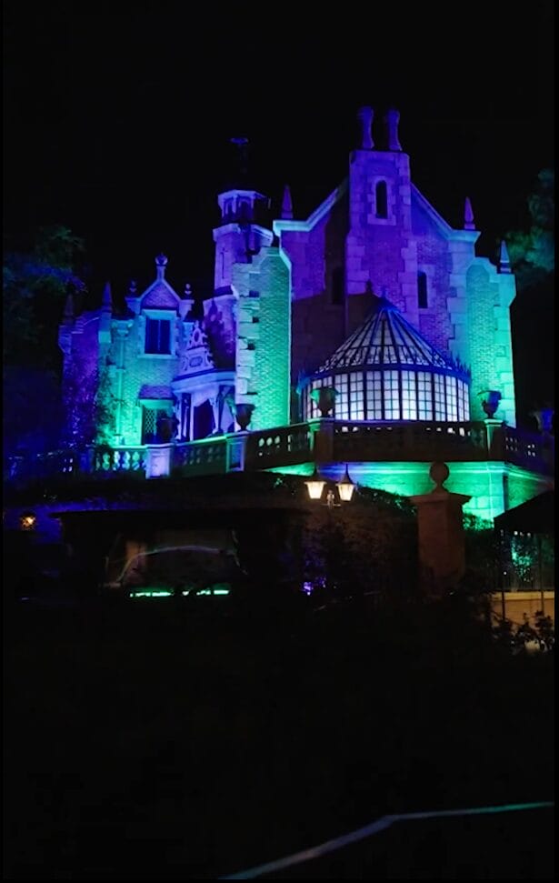 The Haunted Mansion at Walt Disney World glows with green and purple lights at night.