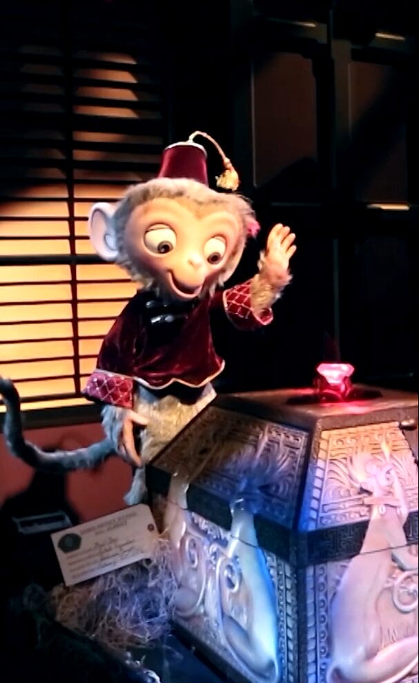 Animatronic of Albert the monkey in a red jacket and fez as he prepares to grab a red jewel from an ornate display in Mystic Manor at Hong Kong Disneyland.