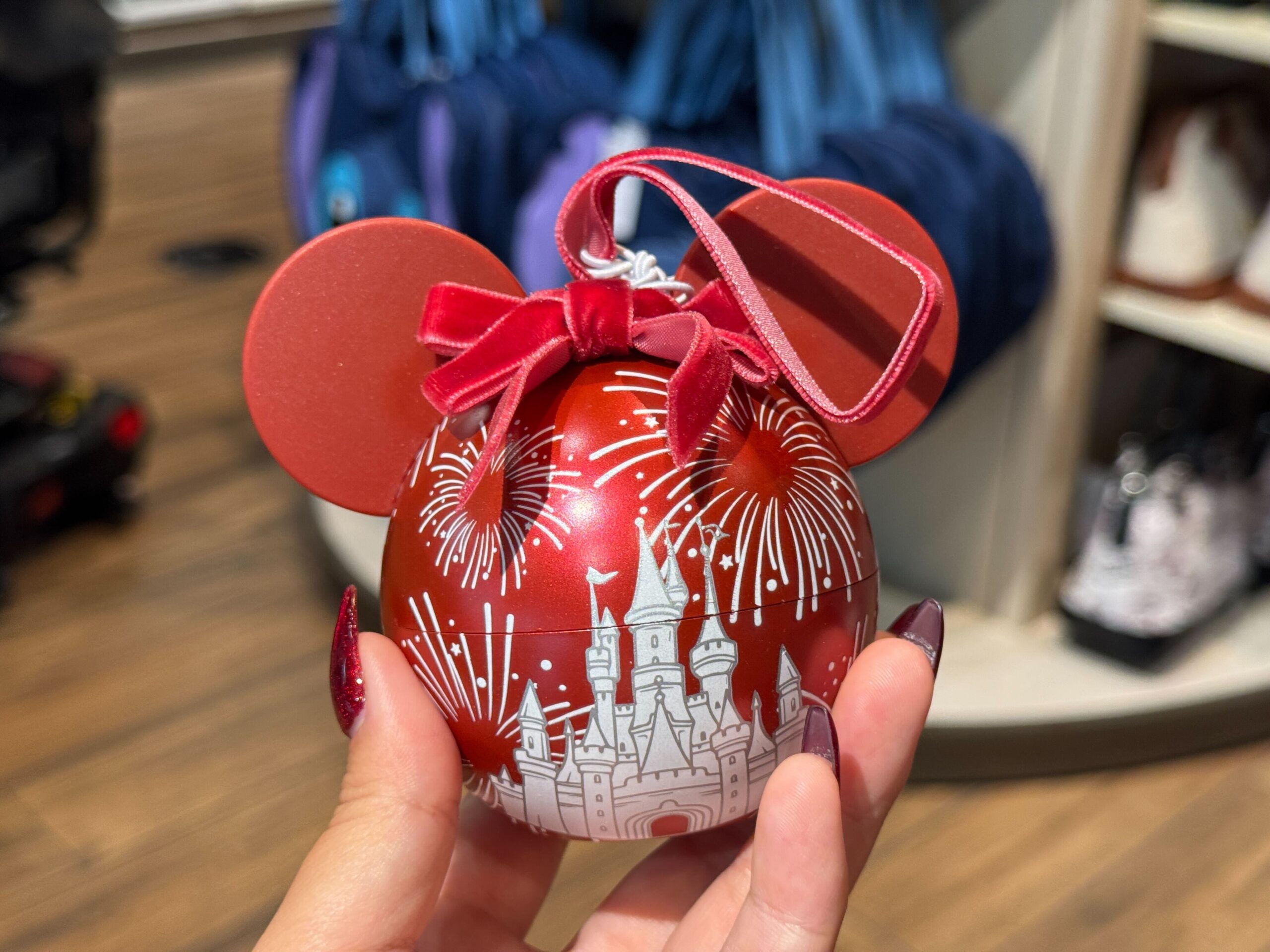 Red Mickey Mouse ornament with castle, fireworks, and 2025 Walt Disney World Christmas merchandise design on store display.