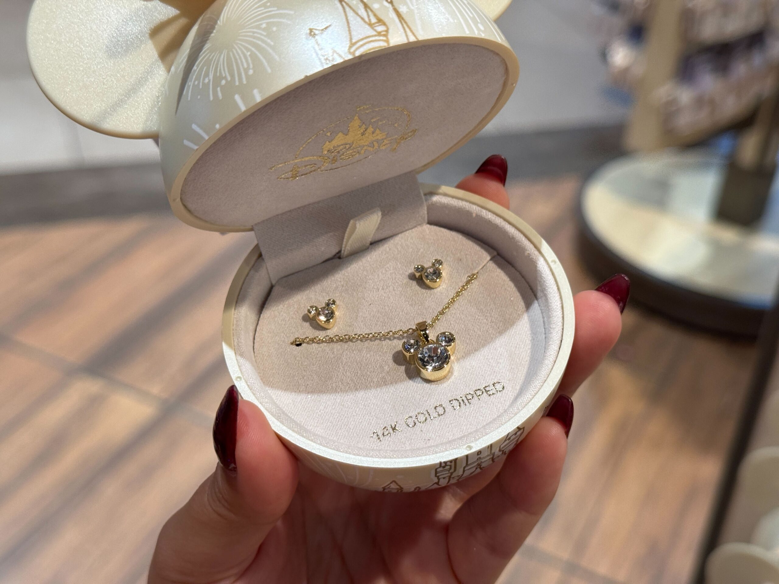 A hand holds a 14k gold Mickey Mouse necklace and earrings set, exclusive Walt Disney World Christmas merchandise.