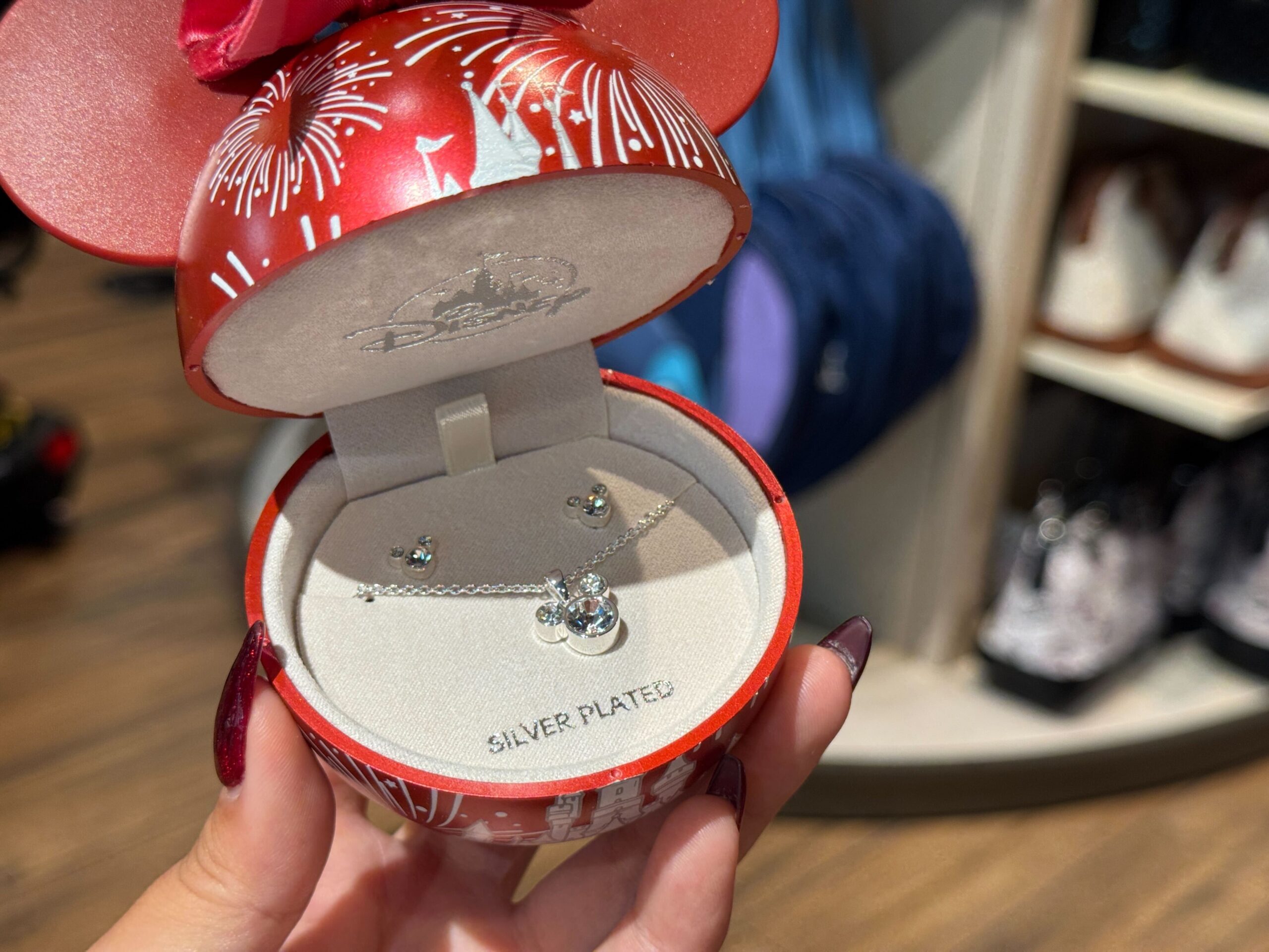 Hand holding a red Disney World Christmas merchandise box with silver plated Mickey Mouse necklace and earrings inside.