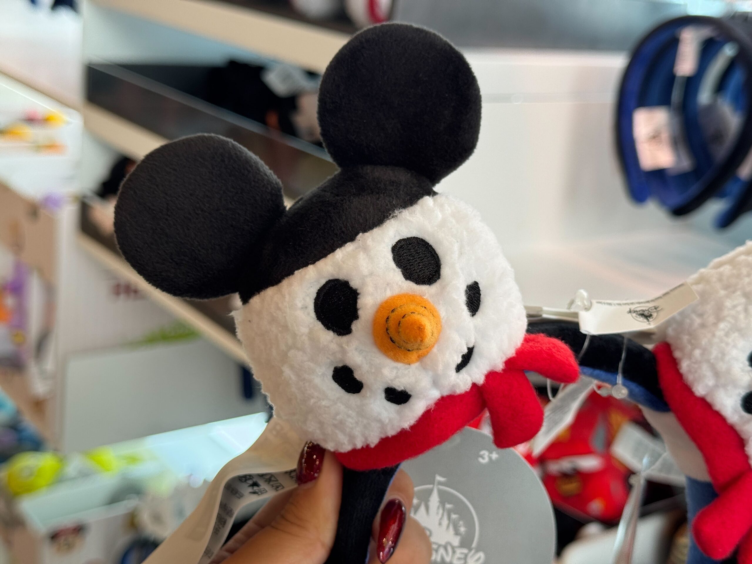 A hand holds a plush toy snowman with Mickey Mouse ears—festive Disney World Christmas merchandise in a store.