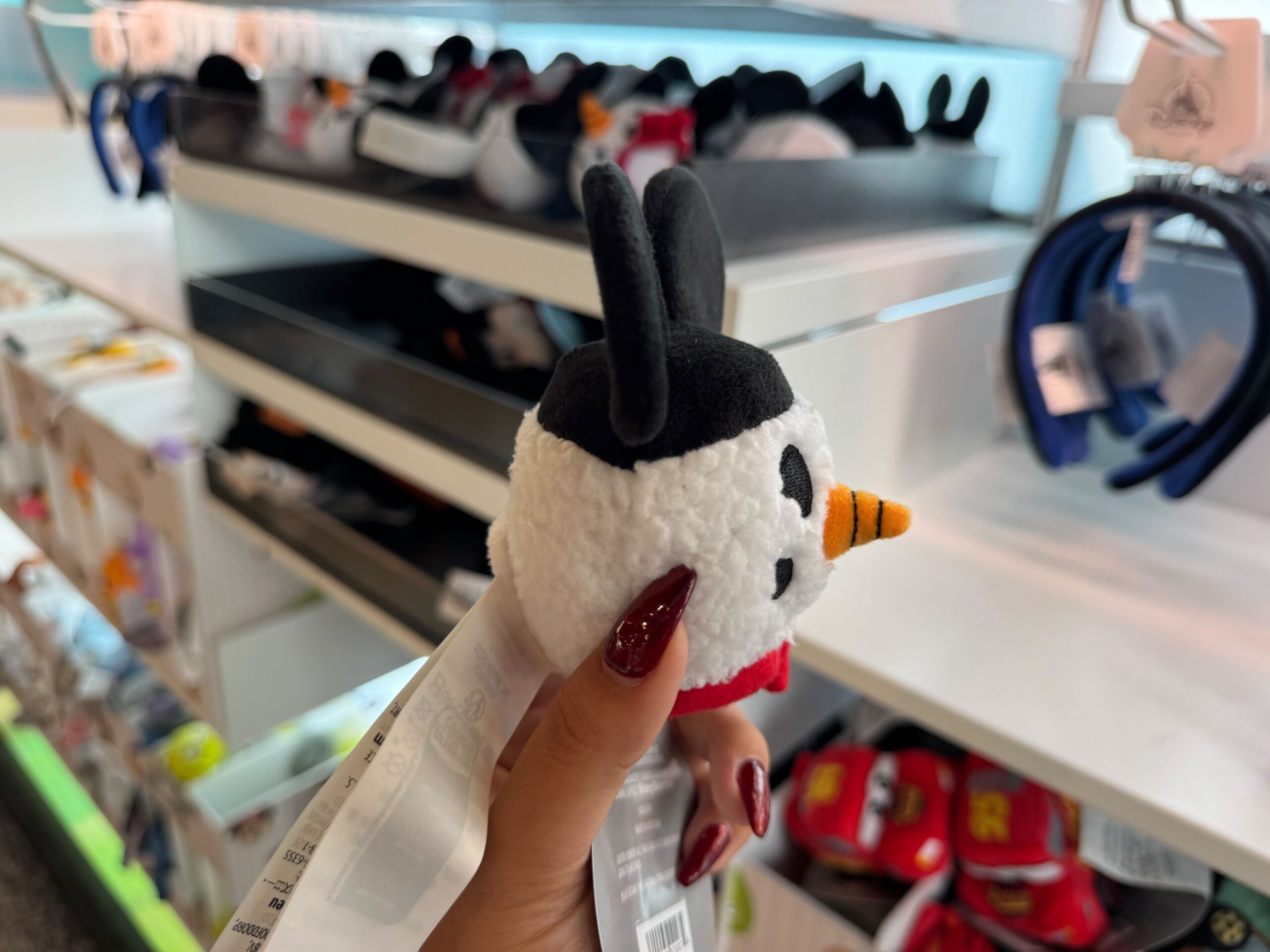 A hand holds a plush snowman toy with black ears, part of the 2025 Walt Disney World Christmas merchandise collection.