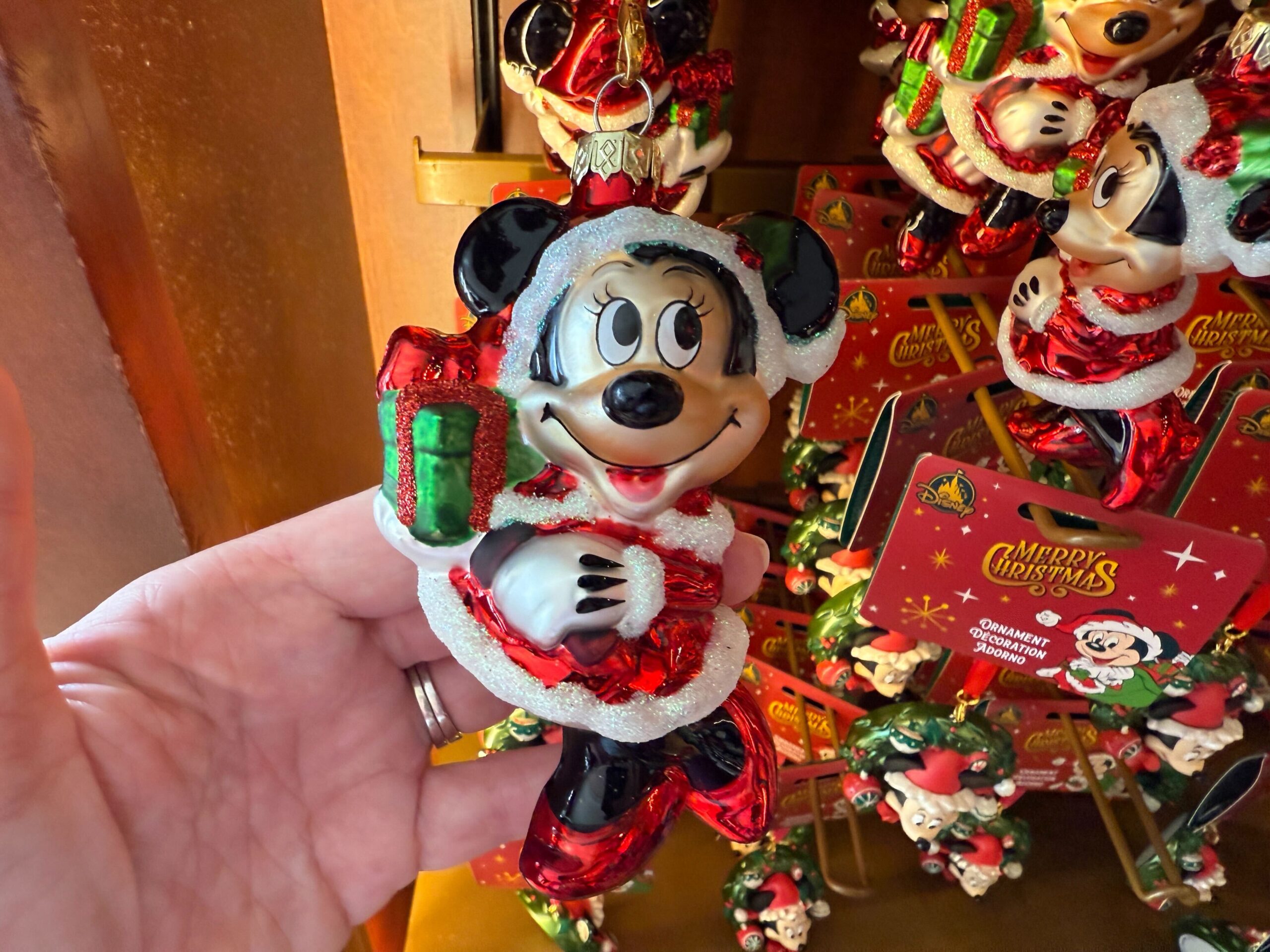 A hand holds a Minnie Mouse Christmas ornament from Walt Disney World, dressed in red with a green gift.