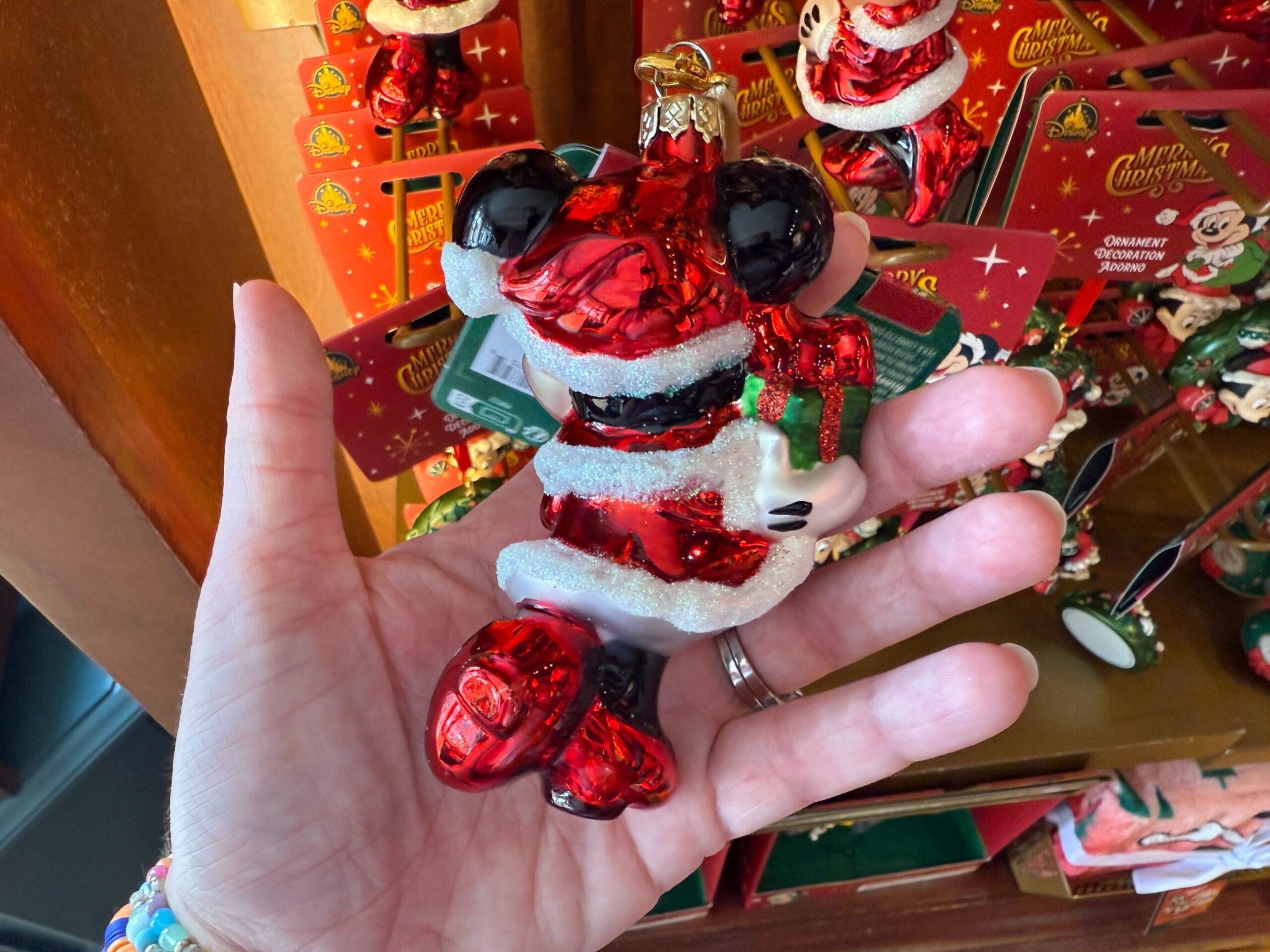A hand holds a shiny, red and white Mickey Mouse Santa ornament—festive 2025 Christmas merchandise from Walt Disney World.