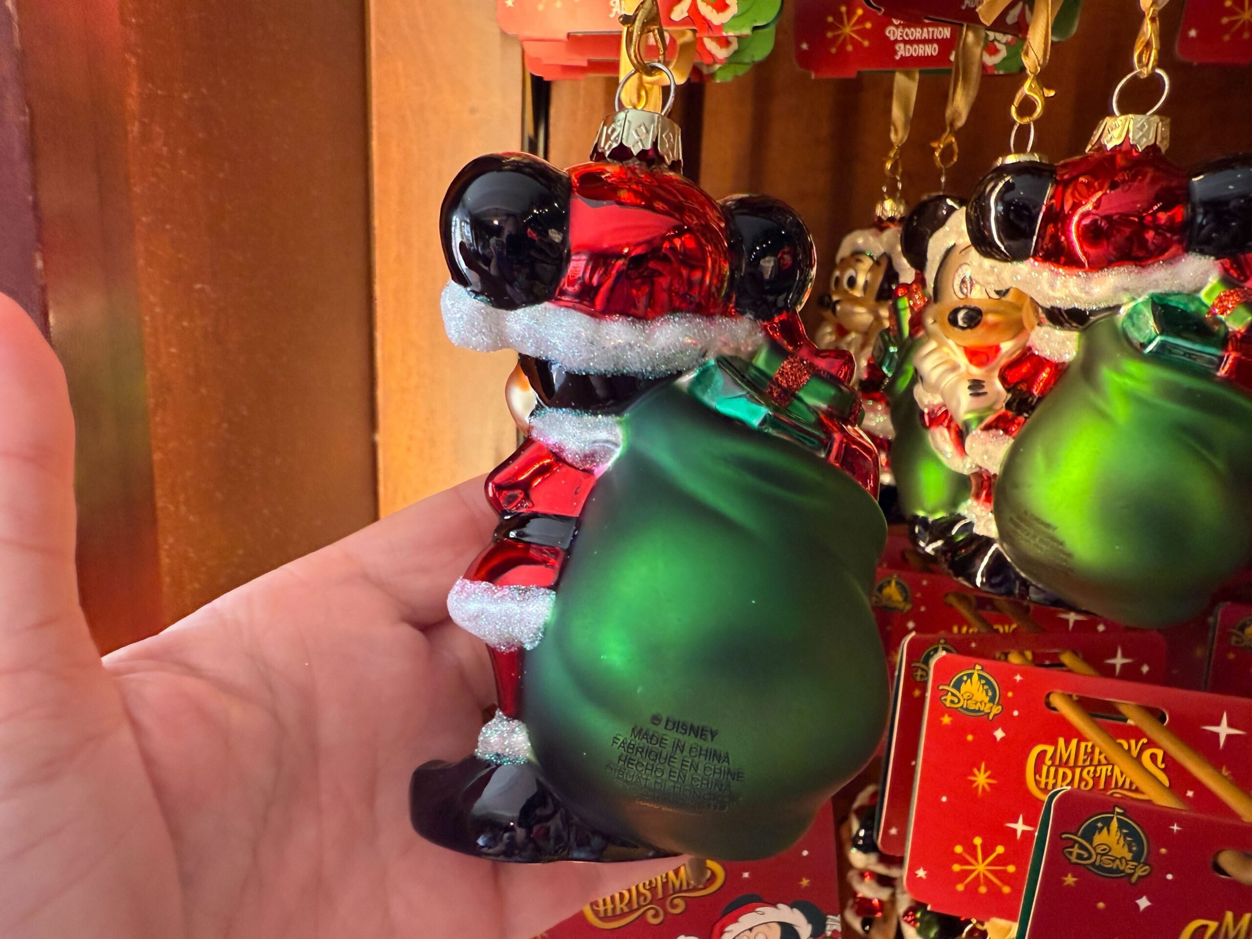 A hand holds a 2025 Walt Disney World Mickey Mouse Christmas ornament dressed as Santa with a green sack.