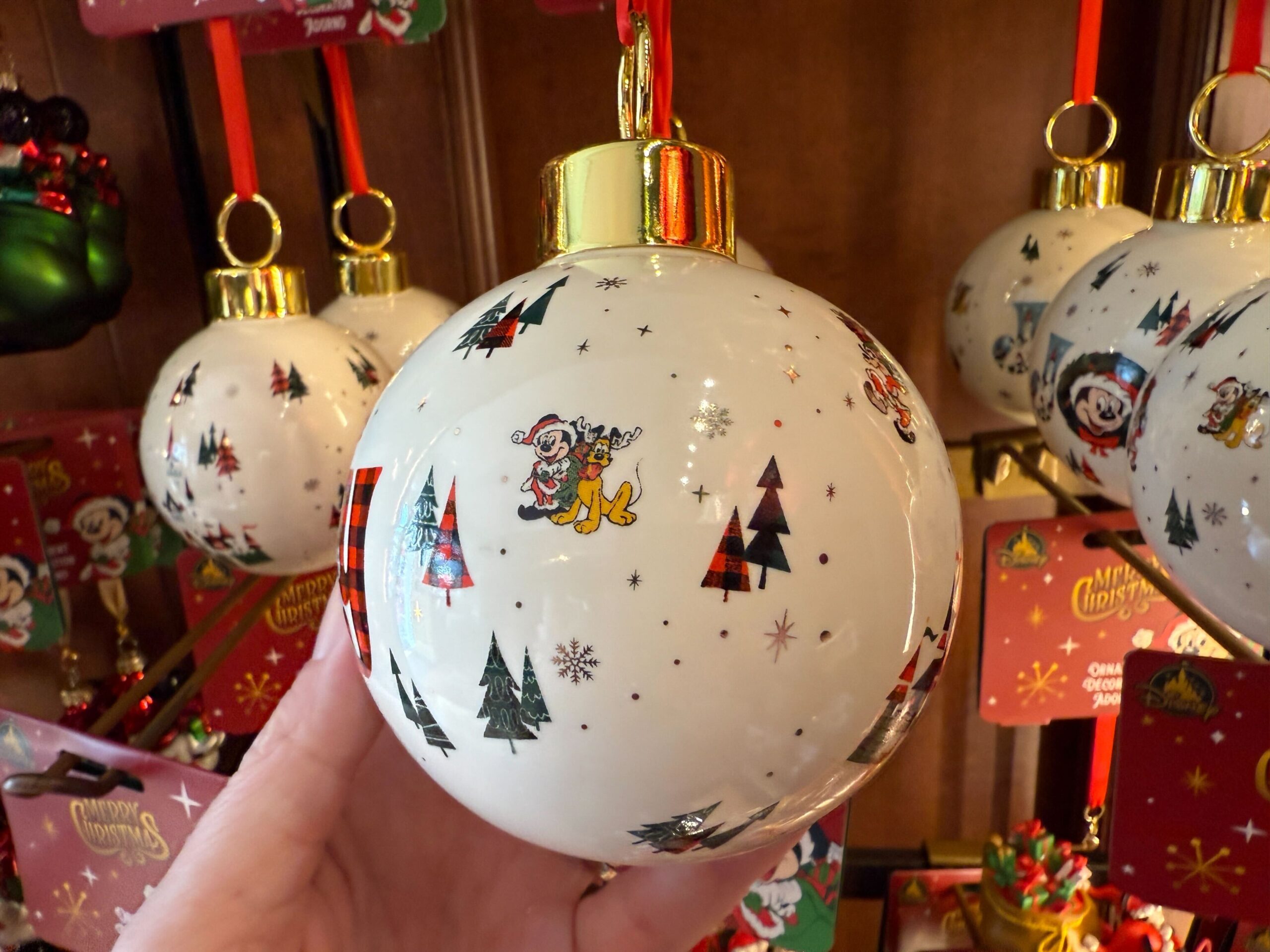 Hand holding a 2025 Walt Disney World Christmas ornament with Mickey, Minnie, trees, and snowflakes, hanging with others.