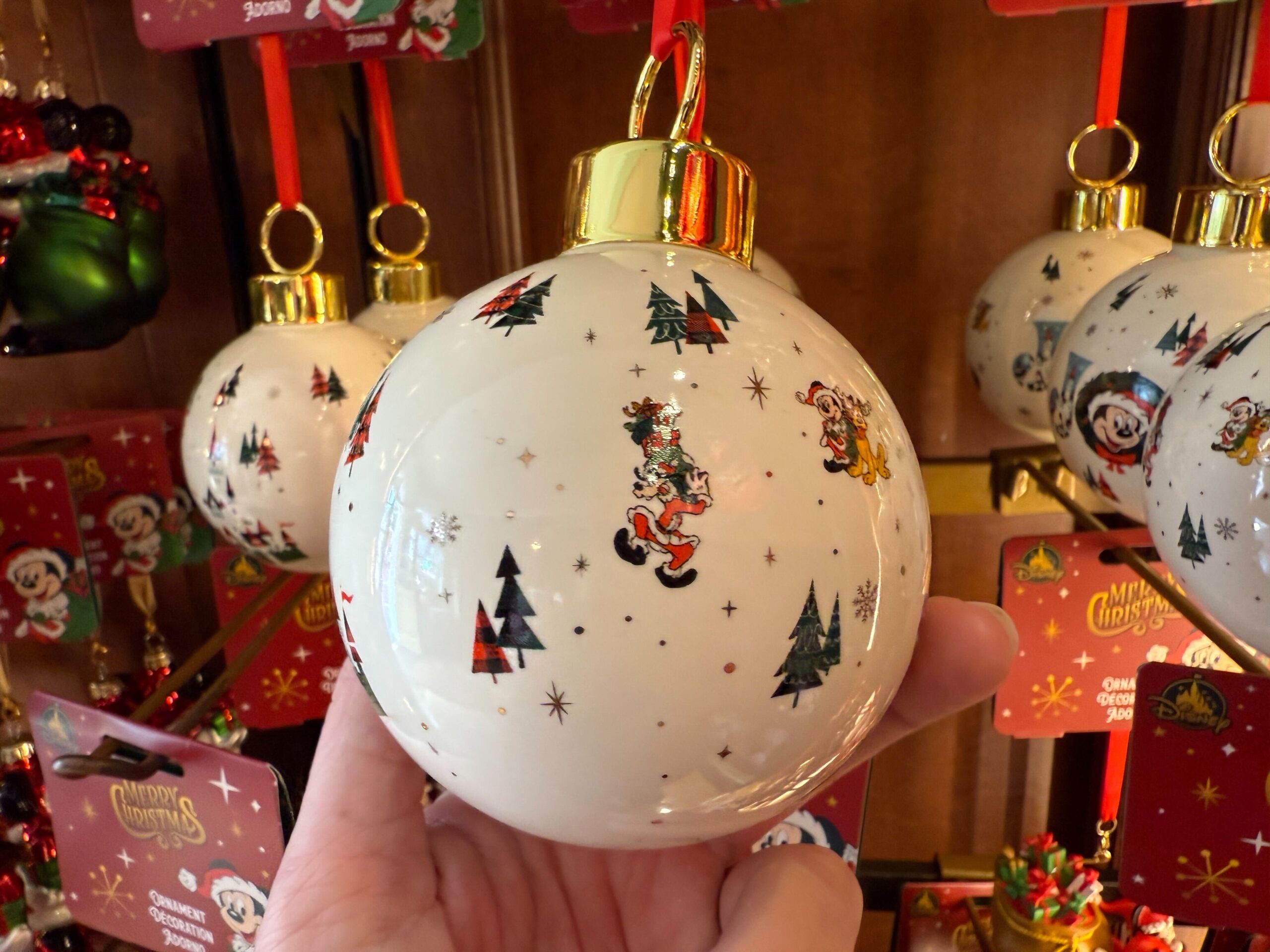 A hand holds a 2025 Walt Disney World Christmas ornament with festive cartoon designs, trees, and stars.