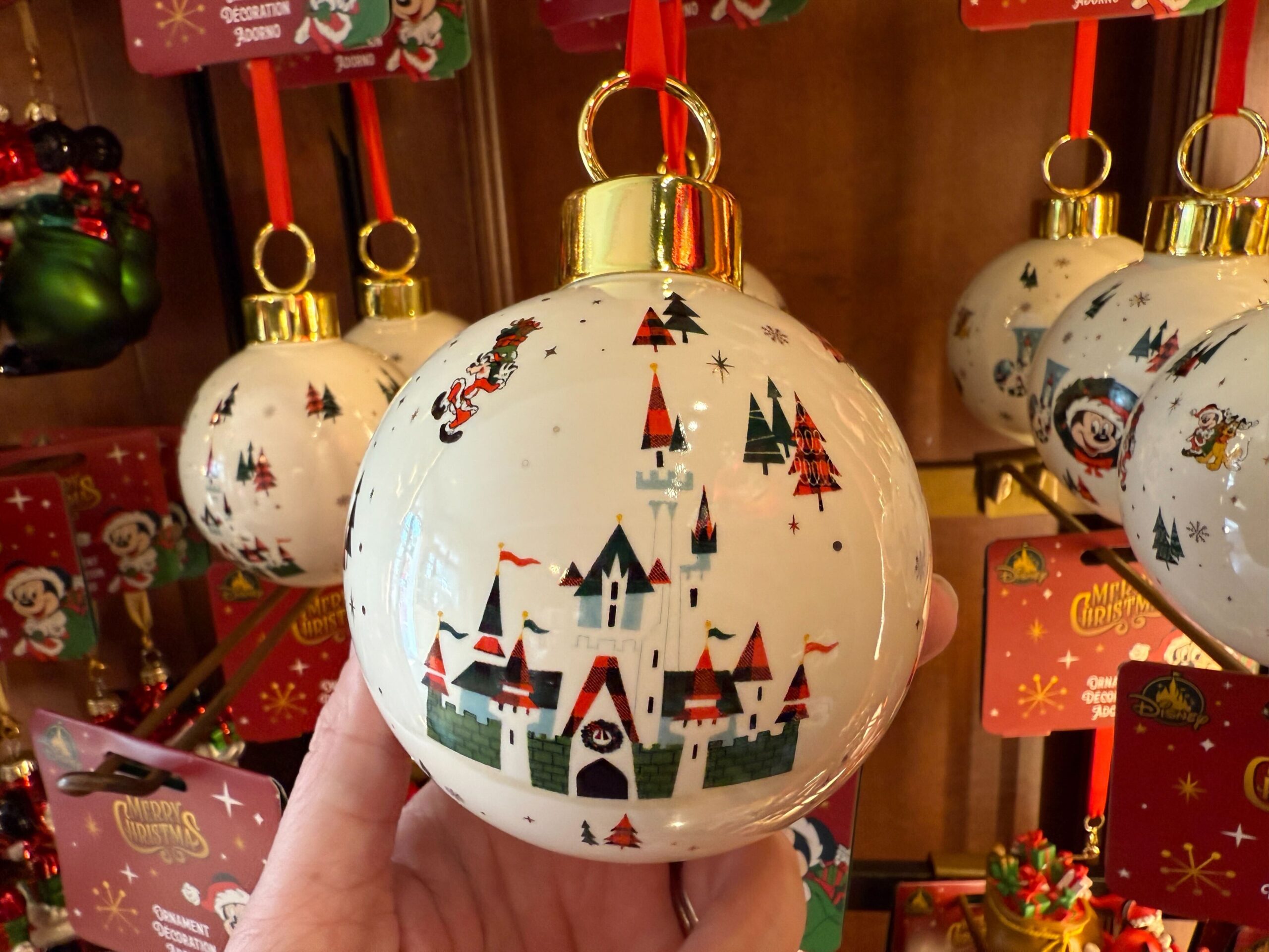 A hand holds a white Walt Disney World Christmas ornament featuring a castle and festive holiday designs.