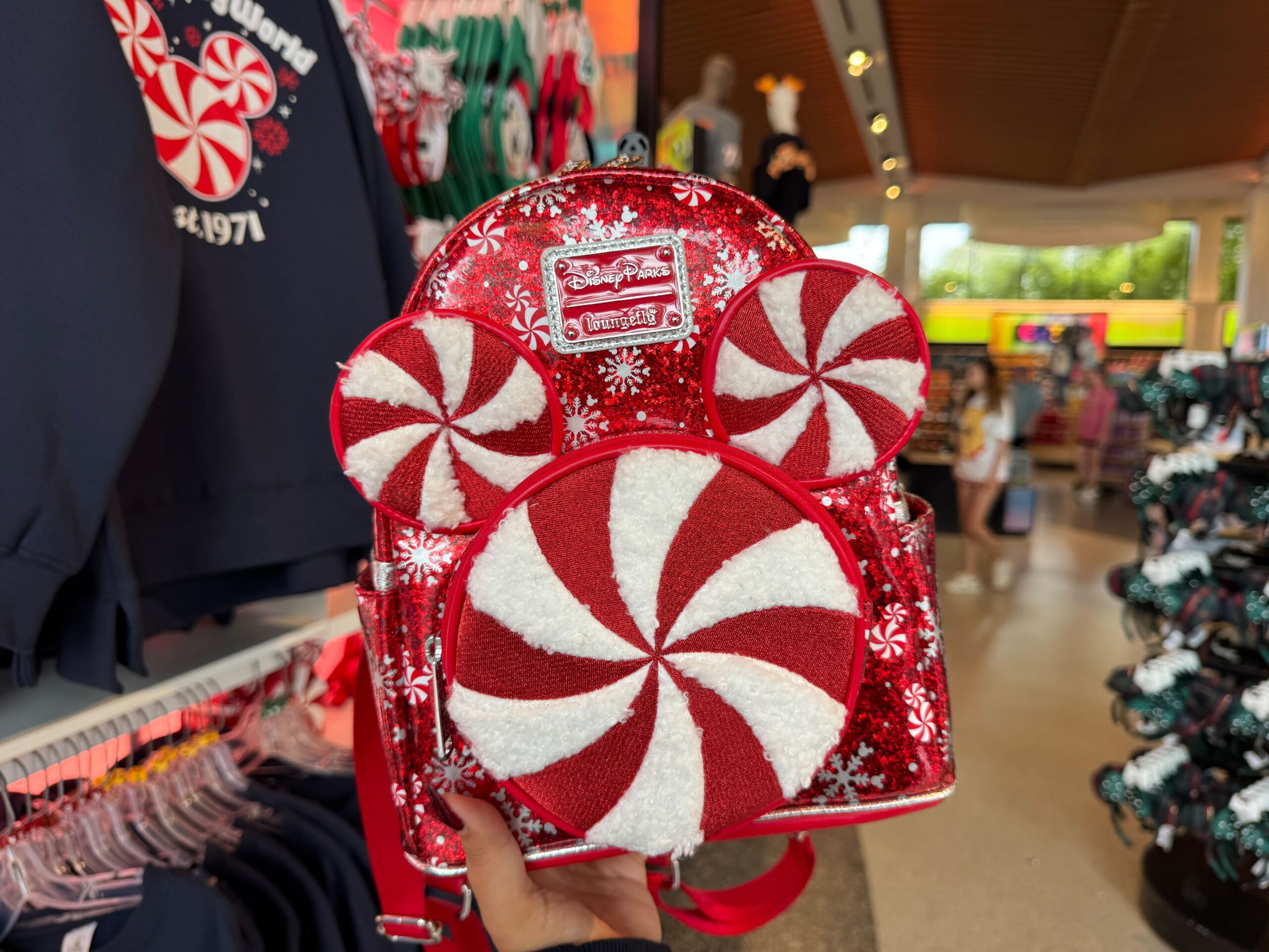 A hand holding a red and white Walt Disney World Christmas merchandise backpack