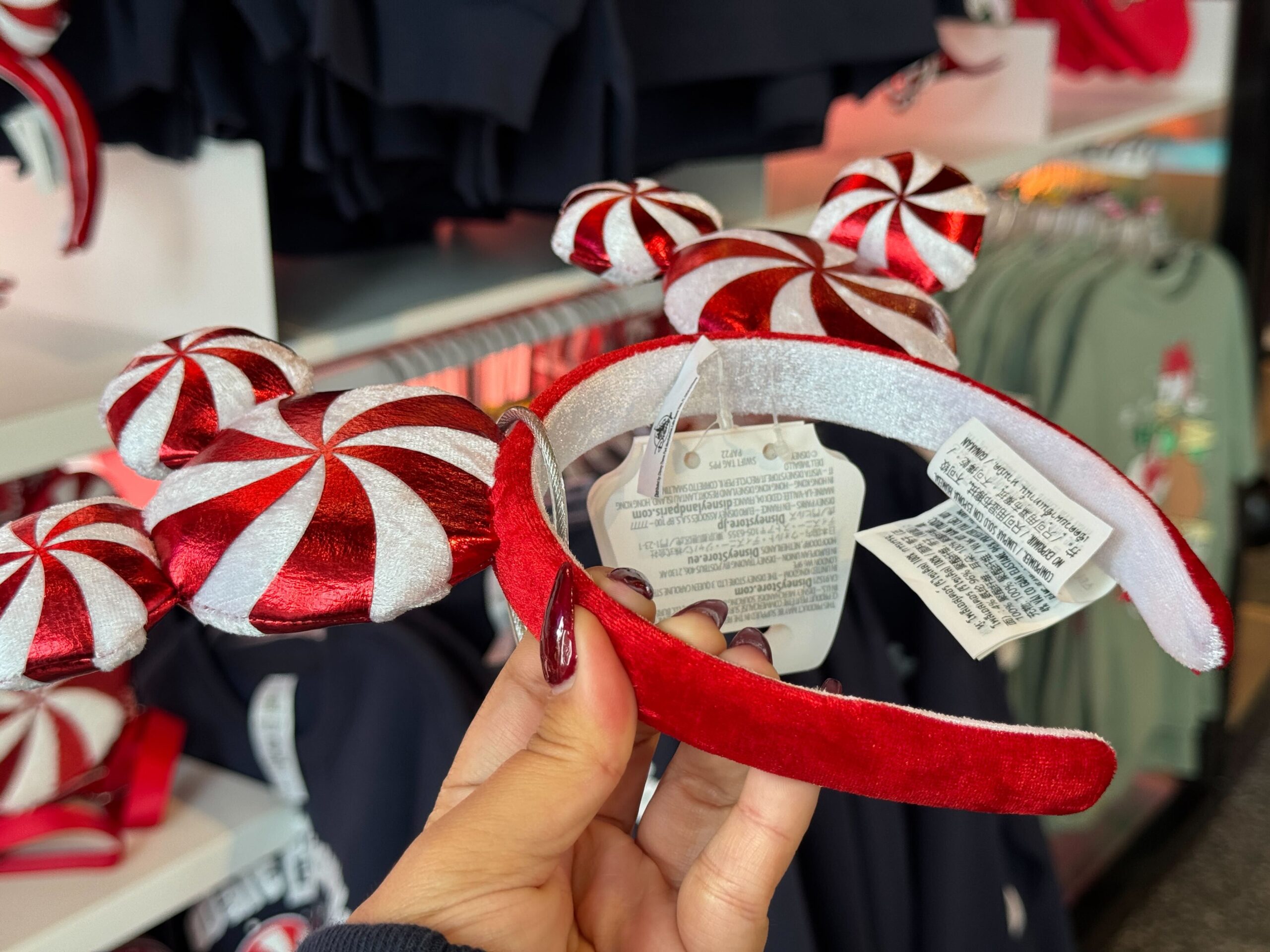 Hand holding a red and white striped peppermint Disney World Christmas merchandise headband in store with clothes in back.
