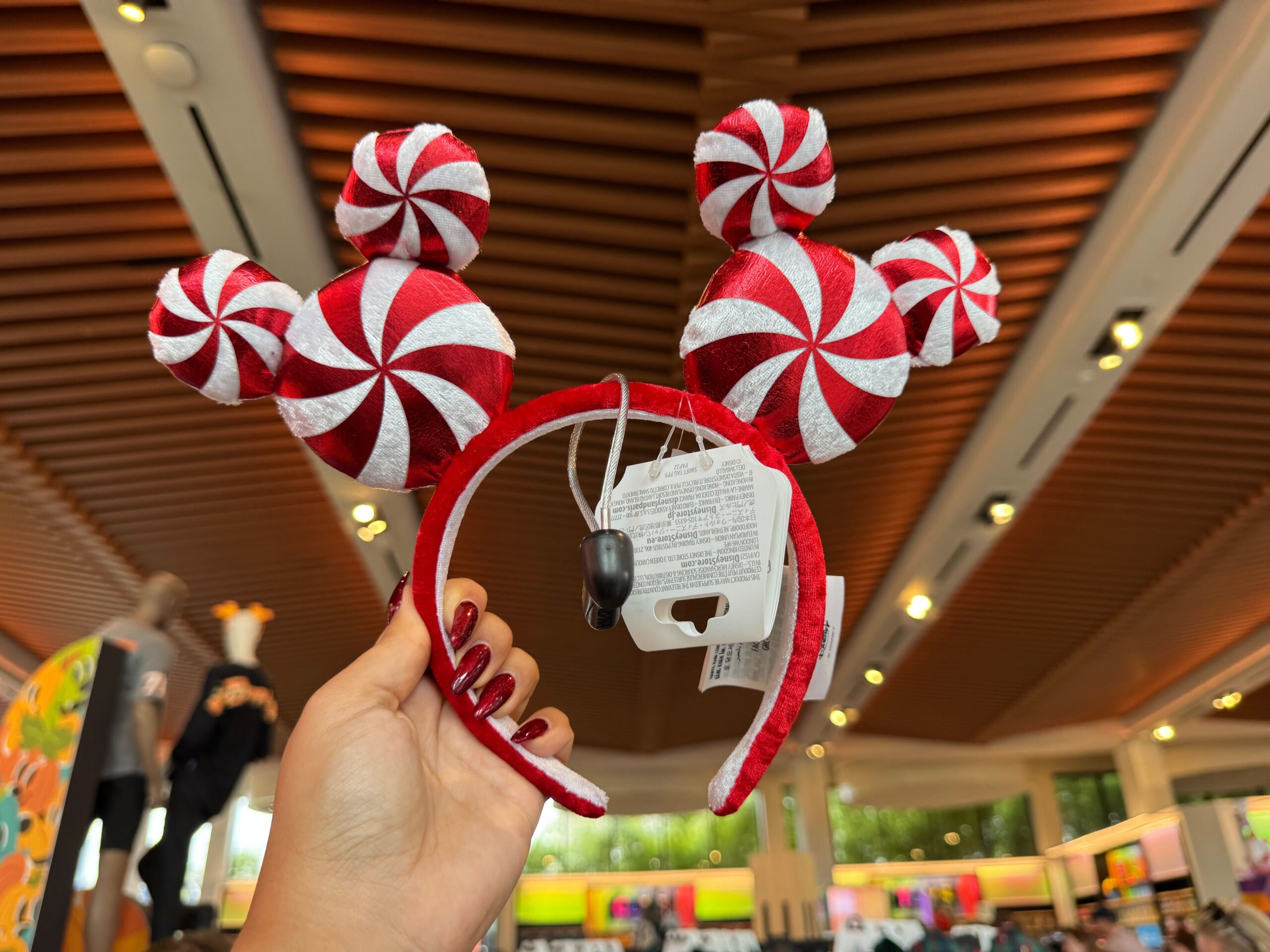 A hand holds a red and white peppermint Mickey ears headband—festive 2025 Walt Disney World Christmas merchandise.