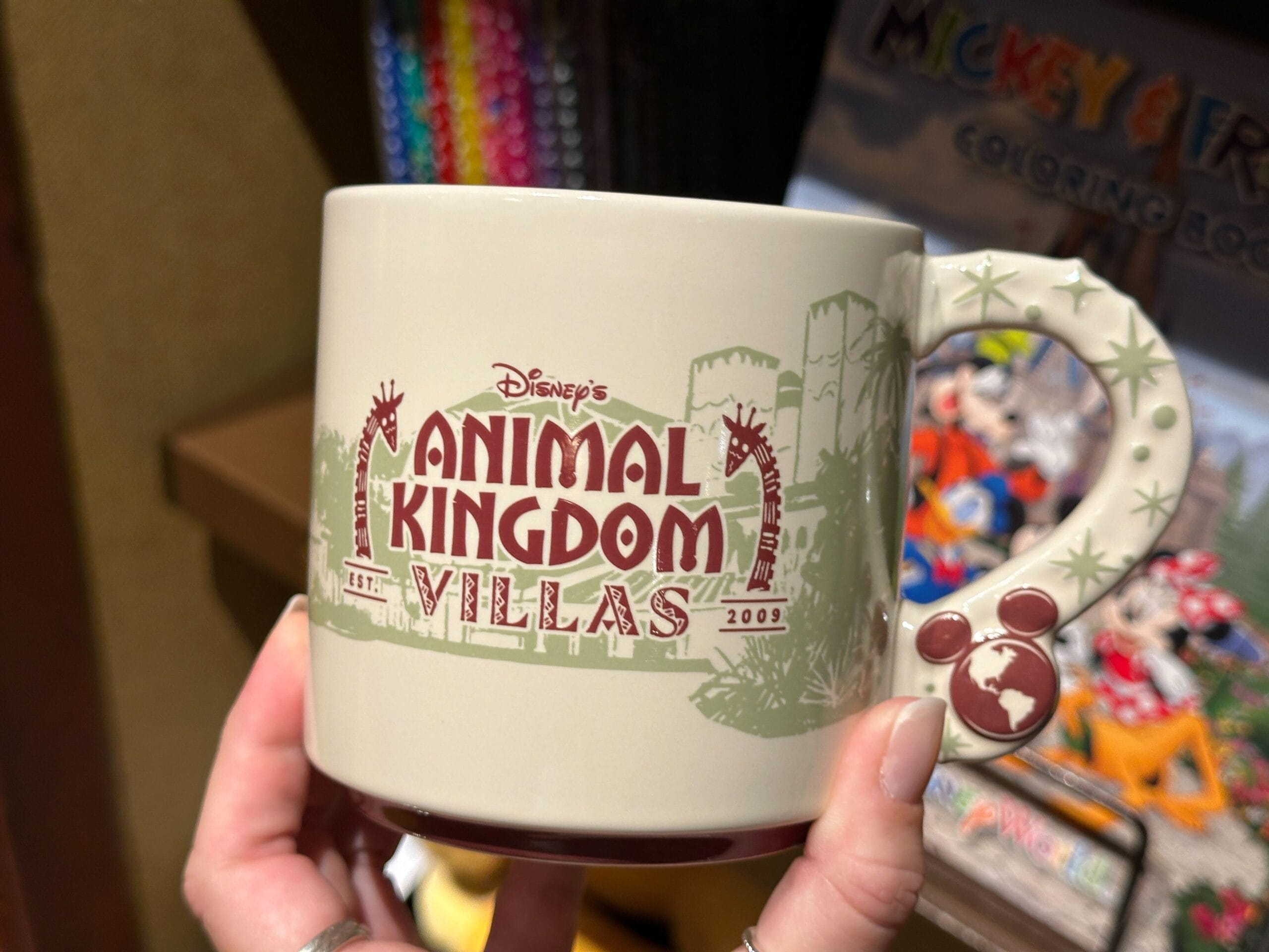 A hand holds a Disney’s Animal Kingdom Villas mug with a Mickey Mouse icon on the handle, no castle like those found in Disney Parks.