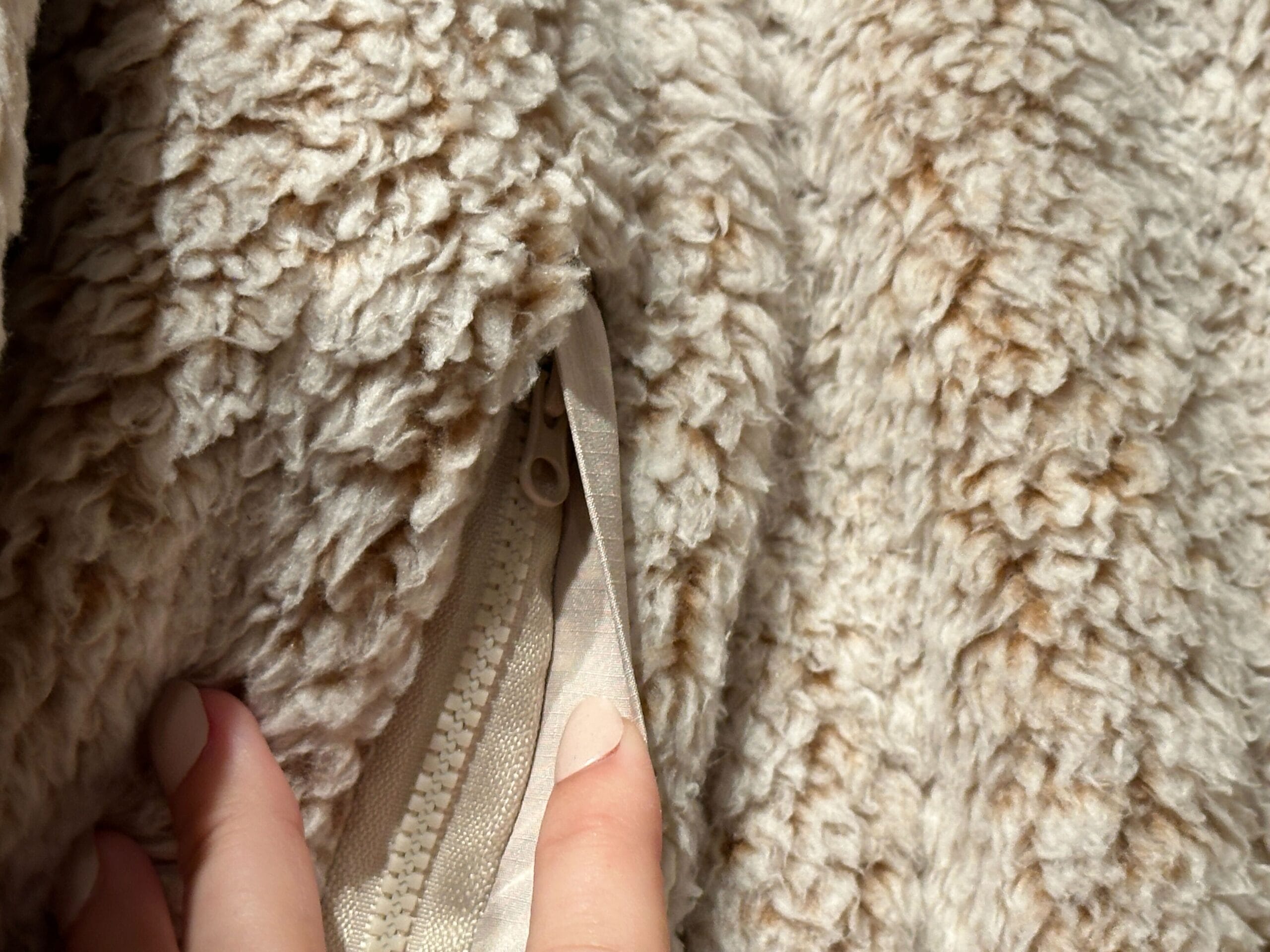 A hand reveals a hidden zipper pocket on beige, fluffy Authentic Original Jackets fabric—no Disney castle here, but cozy as Main Street!