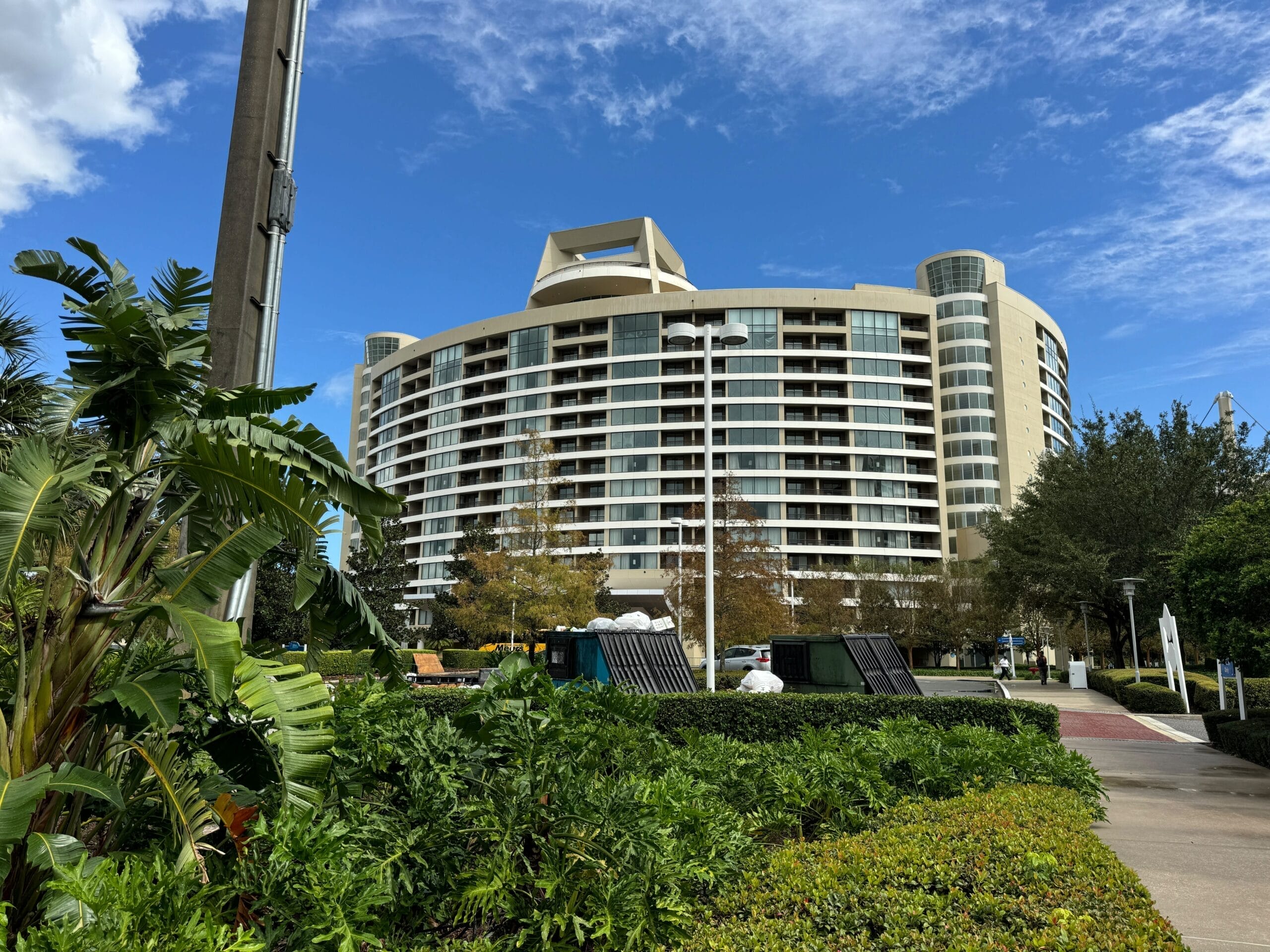 Curved modern hotel with glass balconies, Disney resort style, framed by greenery under a blue sky—not a classic Disney castle.