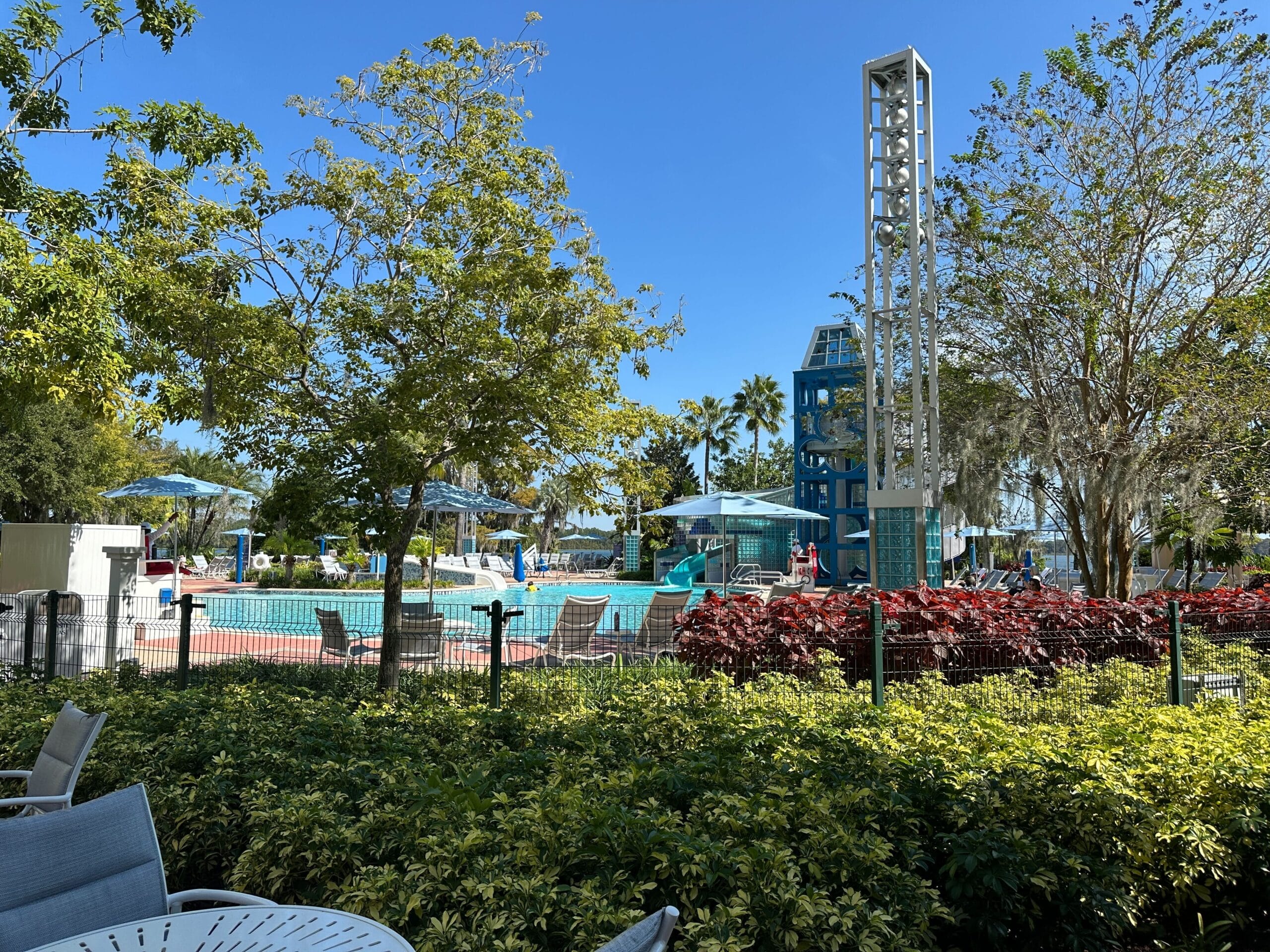 The Contemporary Resort’s outdoor pool with lounge chairs, umbrellas, and trees, just steps away from Magic Kingdom, gleams in the sun.