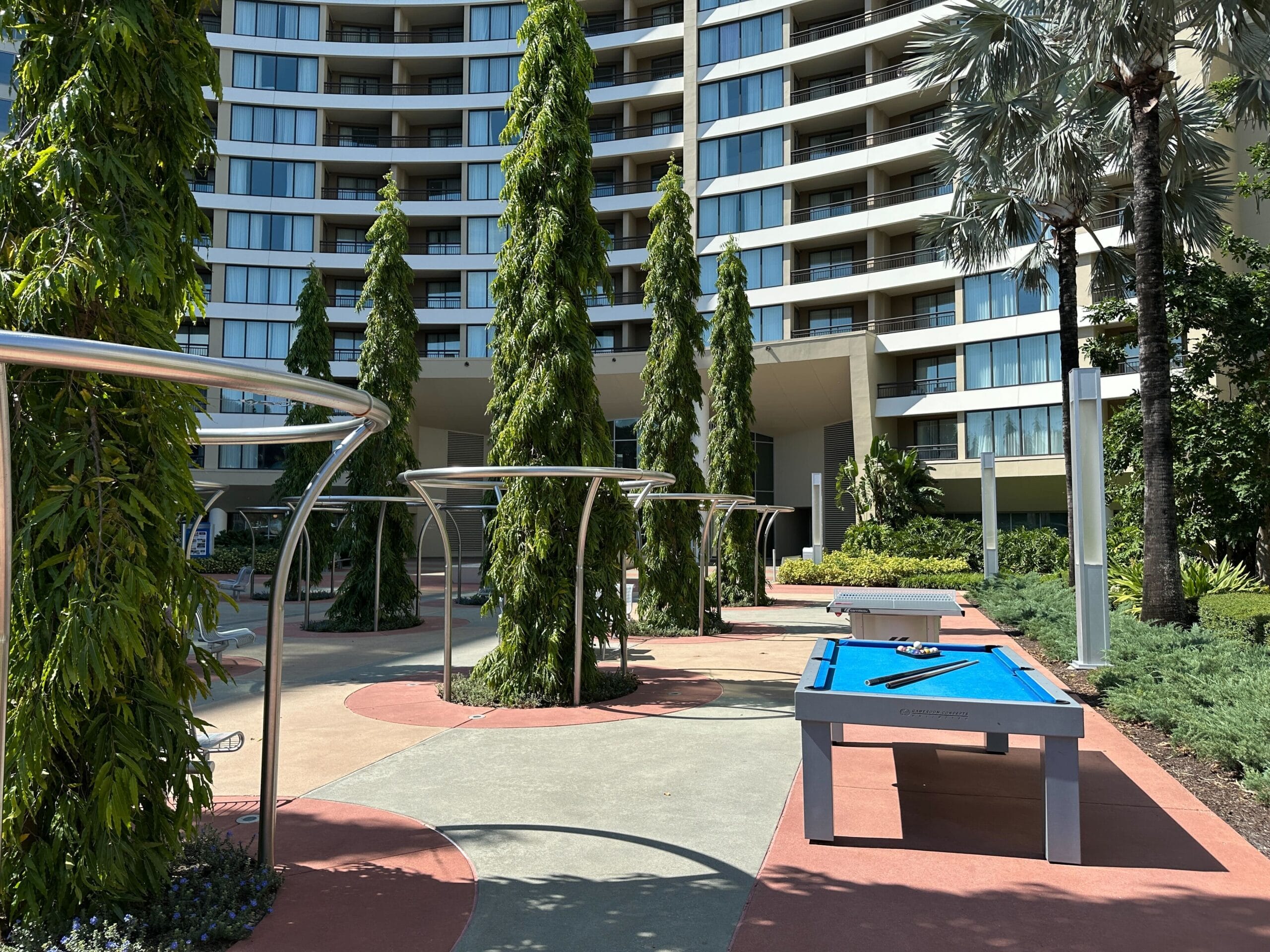 Outdoor recreation area with tall trees and a blue billiards table at Disney's Contemporary Resort, just steps from Magic Kingdom.