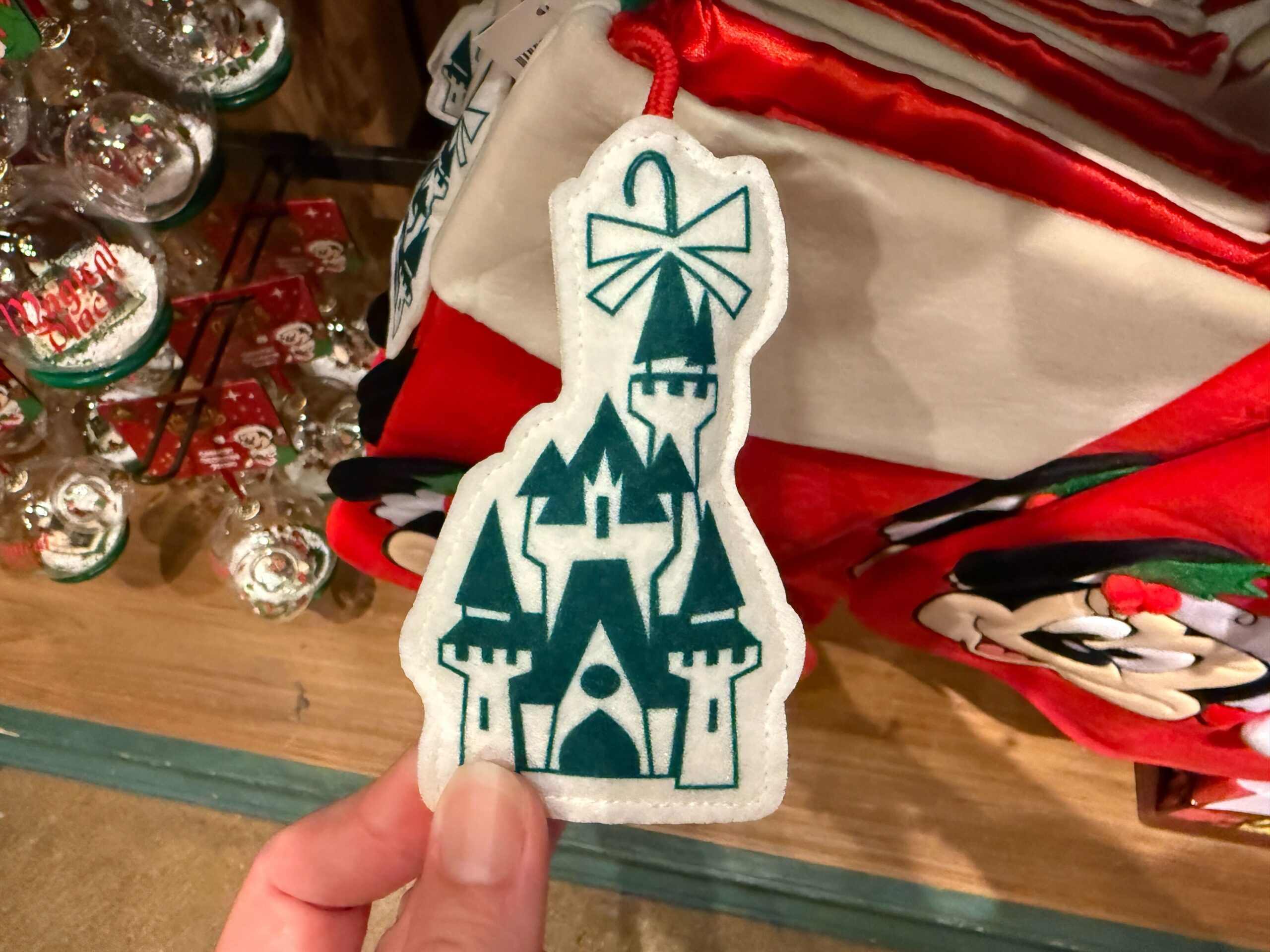 A hand holds a castle-shaped ornament with a bow, featuring 2025 Walt Disney World Christmas merchandise decor.